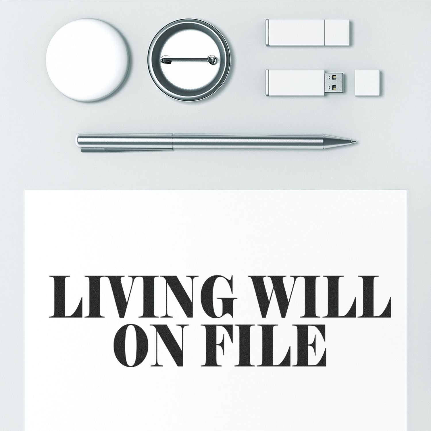 Living Will On File rubber stamp on paper, surrounded by a pen, USB drives, a button, and a round object.