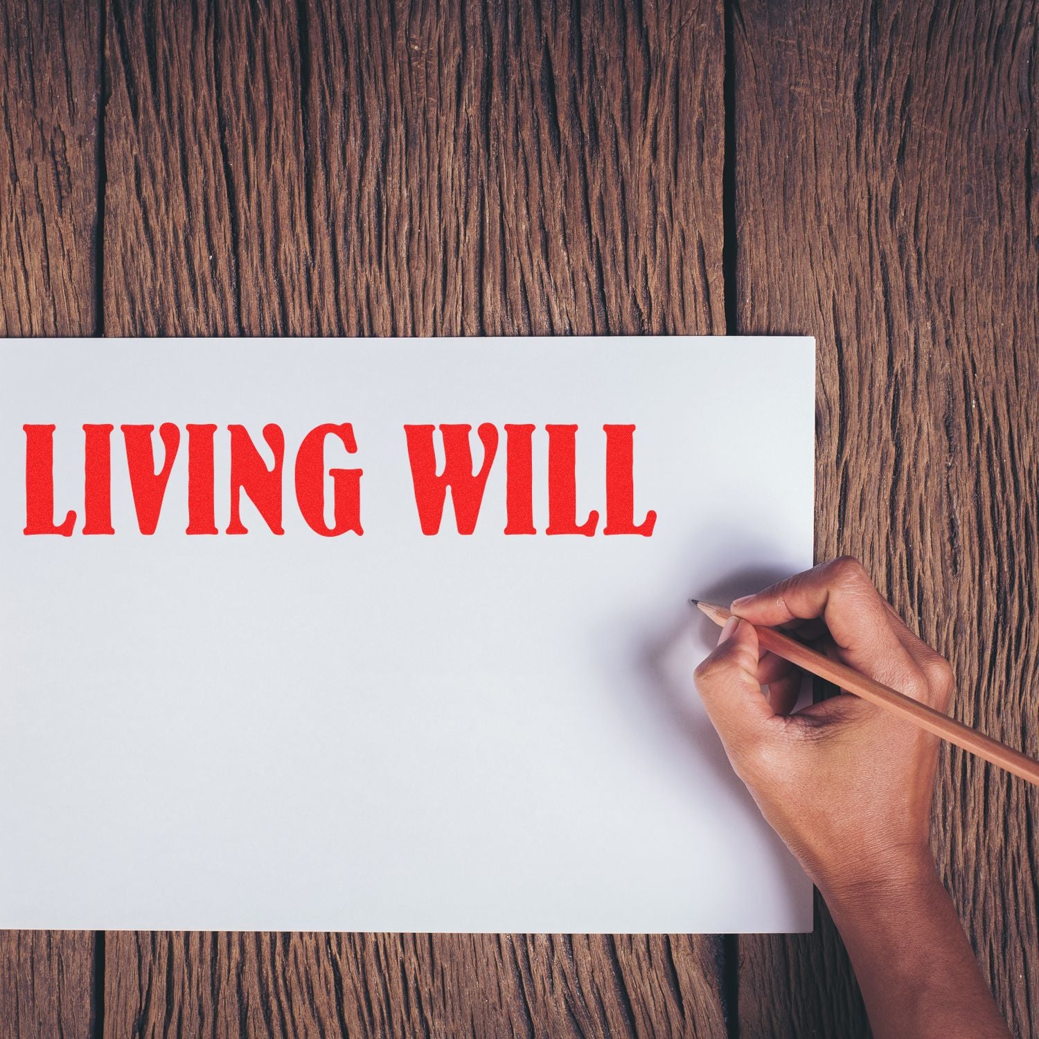 Hand holding a pencil next to a paper stamped with LIVING WILL using a Slim Pre-Inked Living Will Stamp on a wooden surface.