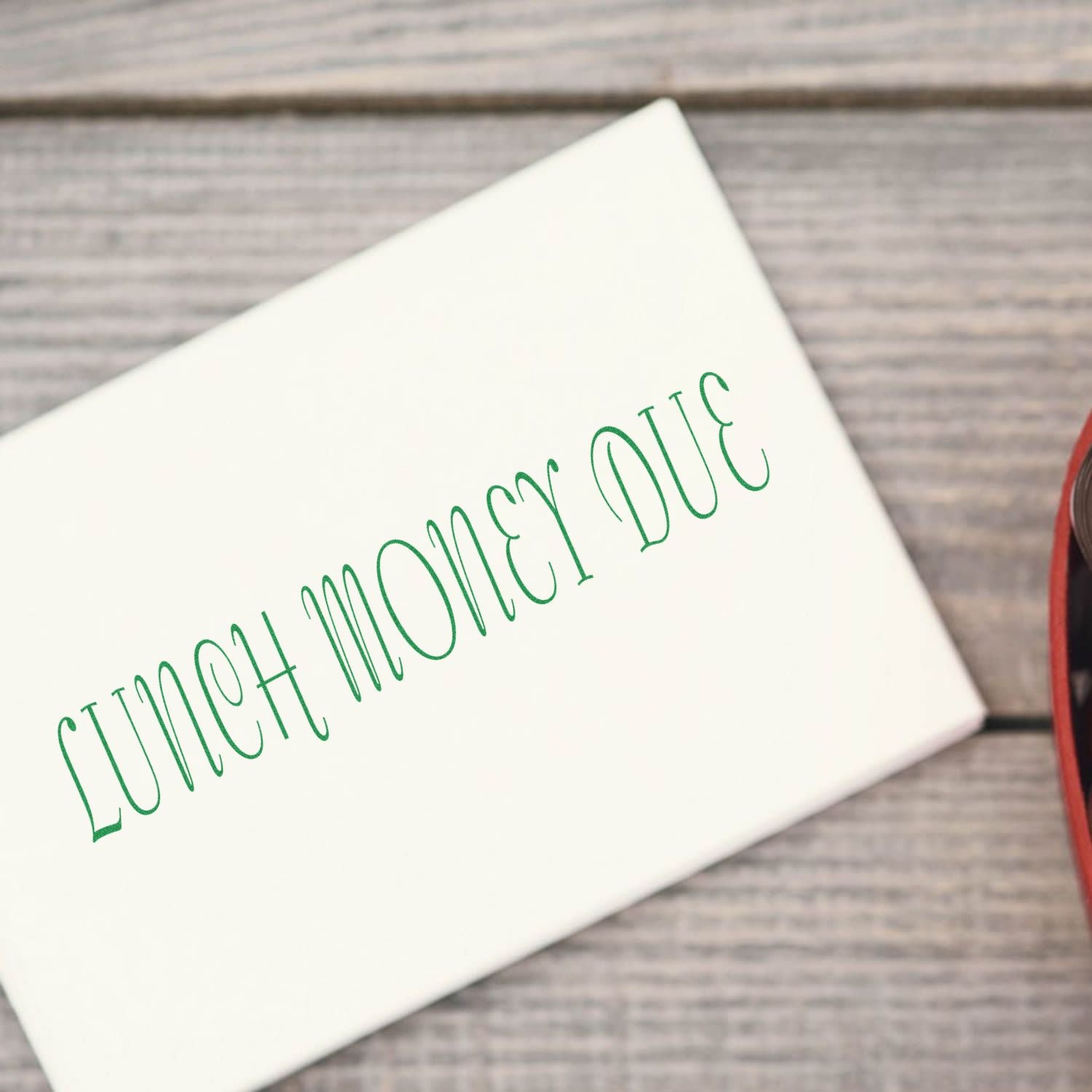 Lunch Money Due rubber stamp on a white envelope placed on a wooden surface next to a red and black object.