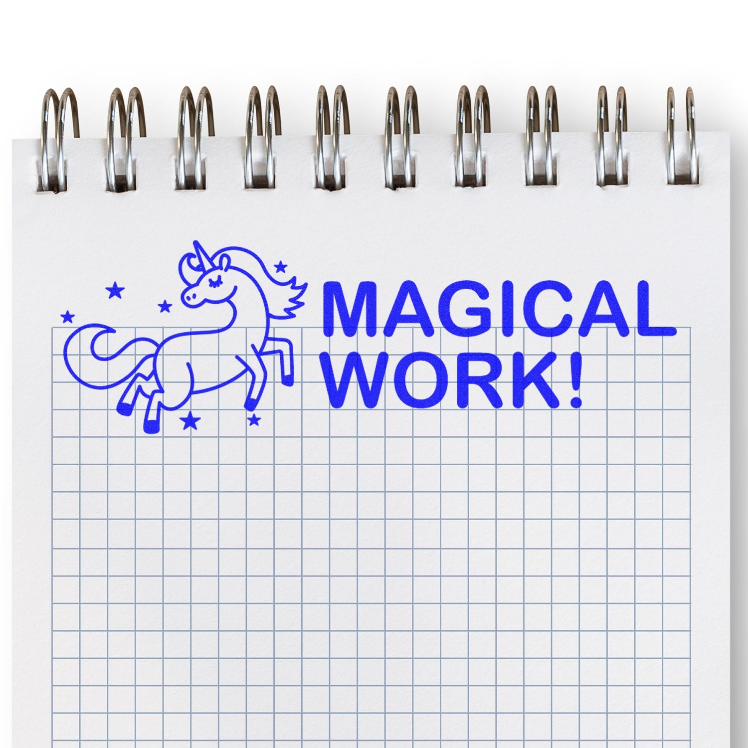 A notebook with a grid pattern stamped with a blue unicorn and stars, and the text MAGICAL WORK! using a Magical Work Rubber Stamp.