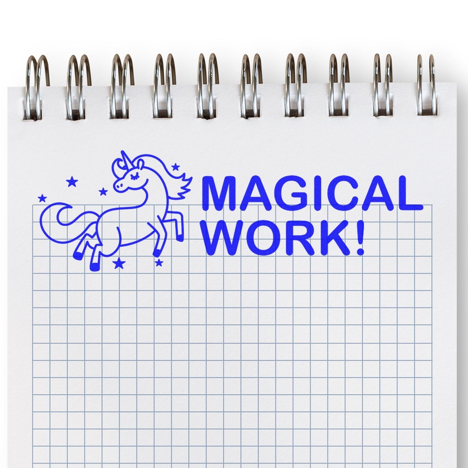 A notebook with a blue grid pattern stamped with a blue unicorn and the text MAGICAL WORK! using the Self Inking Magical Work Stamp.