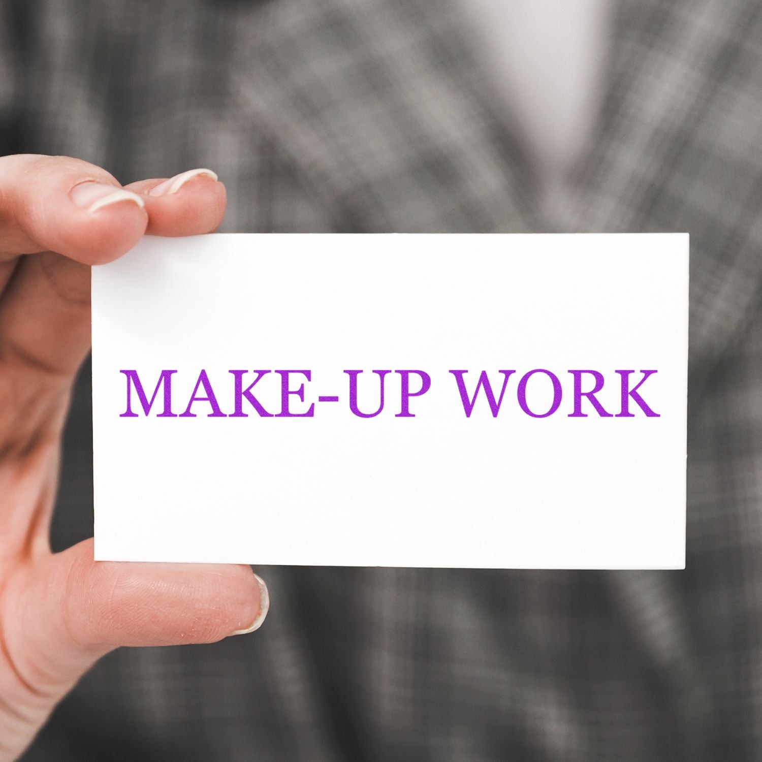 Hand holding a card stamped with MAKE-UP WORK in purple using a Slim Pre-Inked Make Up Work Stamp, against a plaid background.