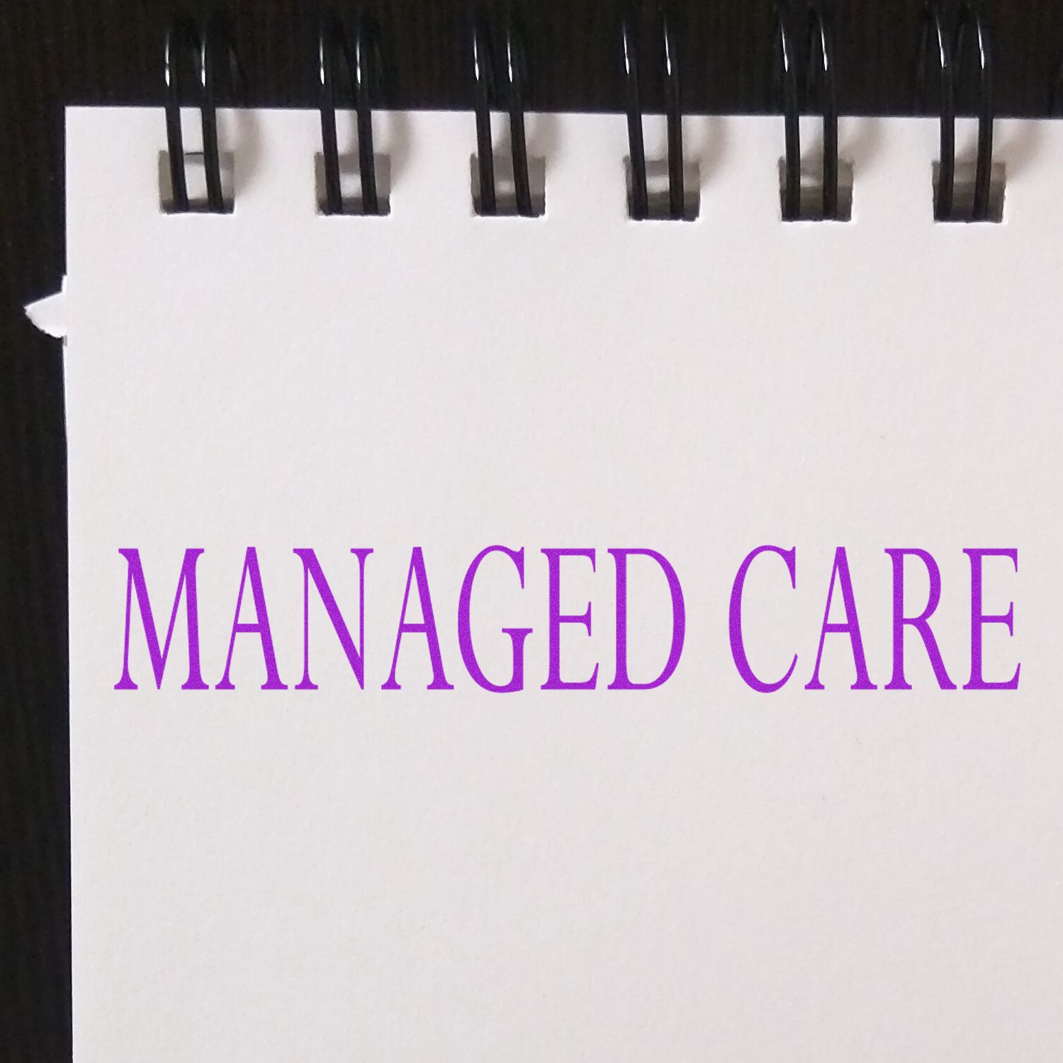 A rubber stamp imprint reading 'MANAGED CARE' in purple ink on a white notepad with a black spiral binding.