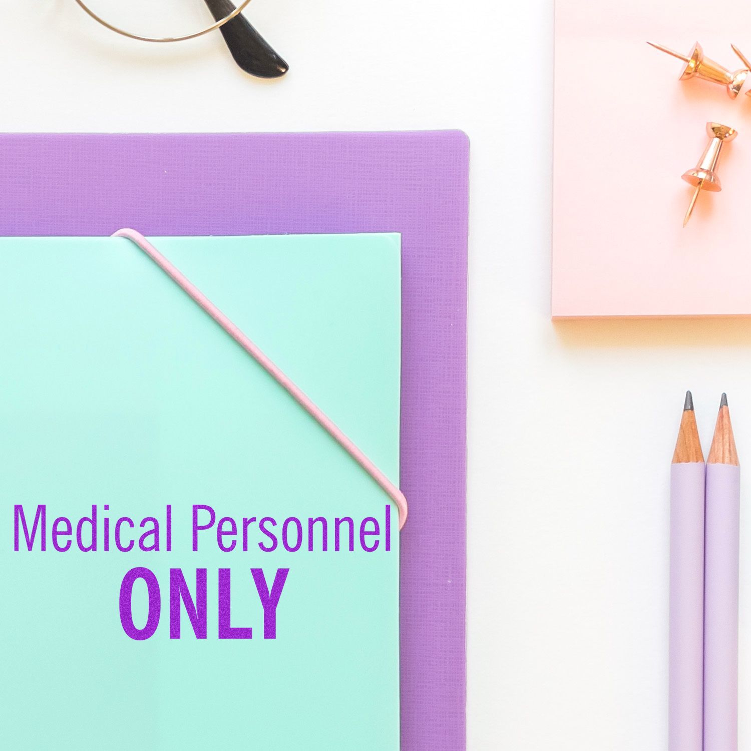 Slim Pre-Inked Medical Personnel Only Stamp used on a mint green folder, surrounded by office supplies on a white desk.