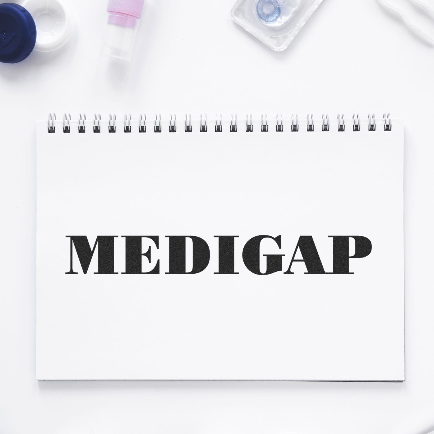 A Self Inking Medigap Stamp imprints the word MEDIGAP on a white spiral notebook, surrounded by office supplies.