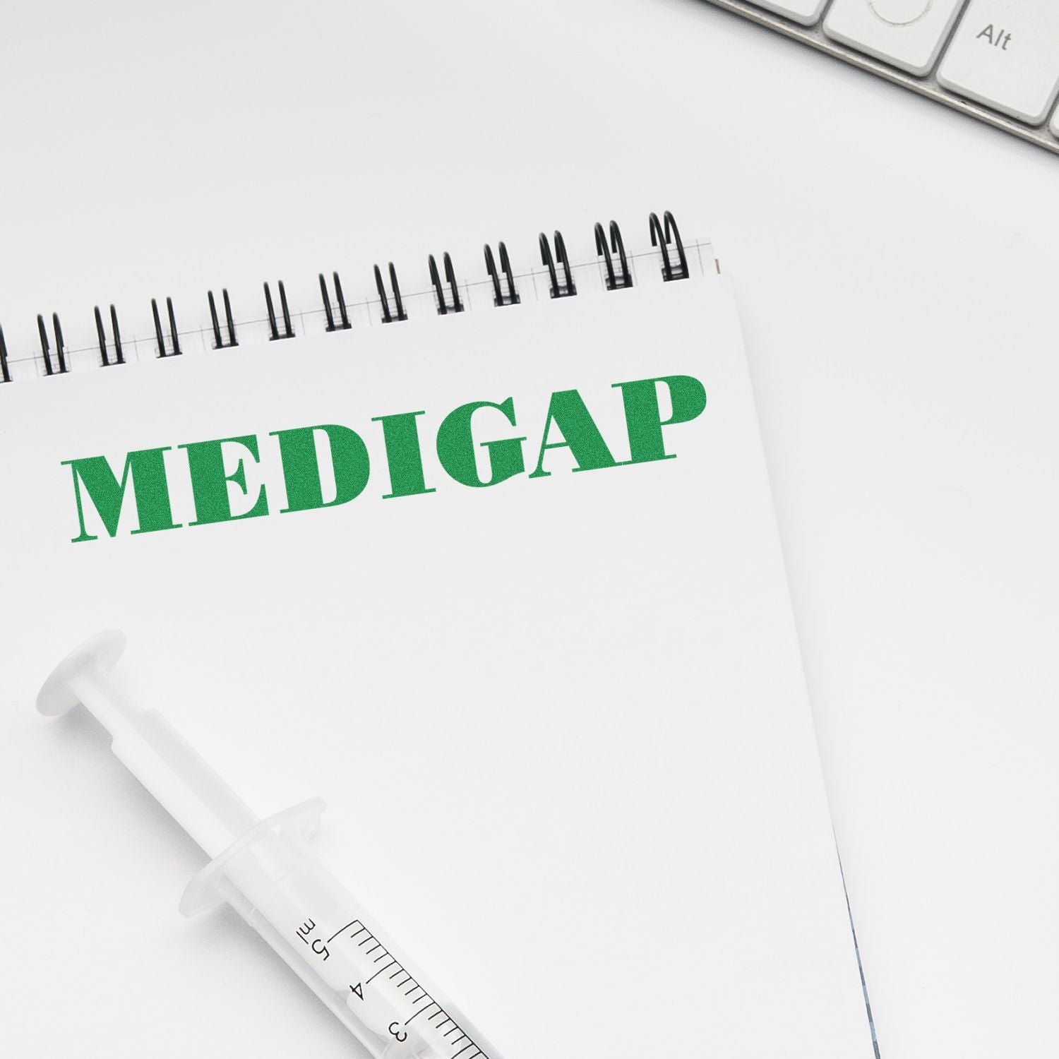 Notebook with MEDIGAP stamped in green using the Large Medigap Rubber Stamp, next to a syringe and a keyboard on a white surface.