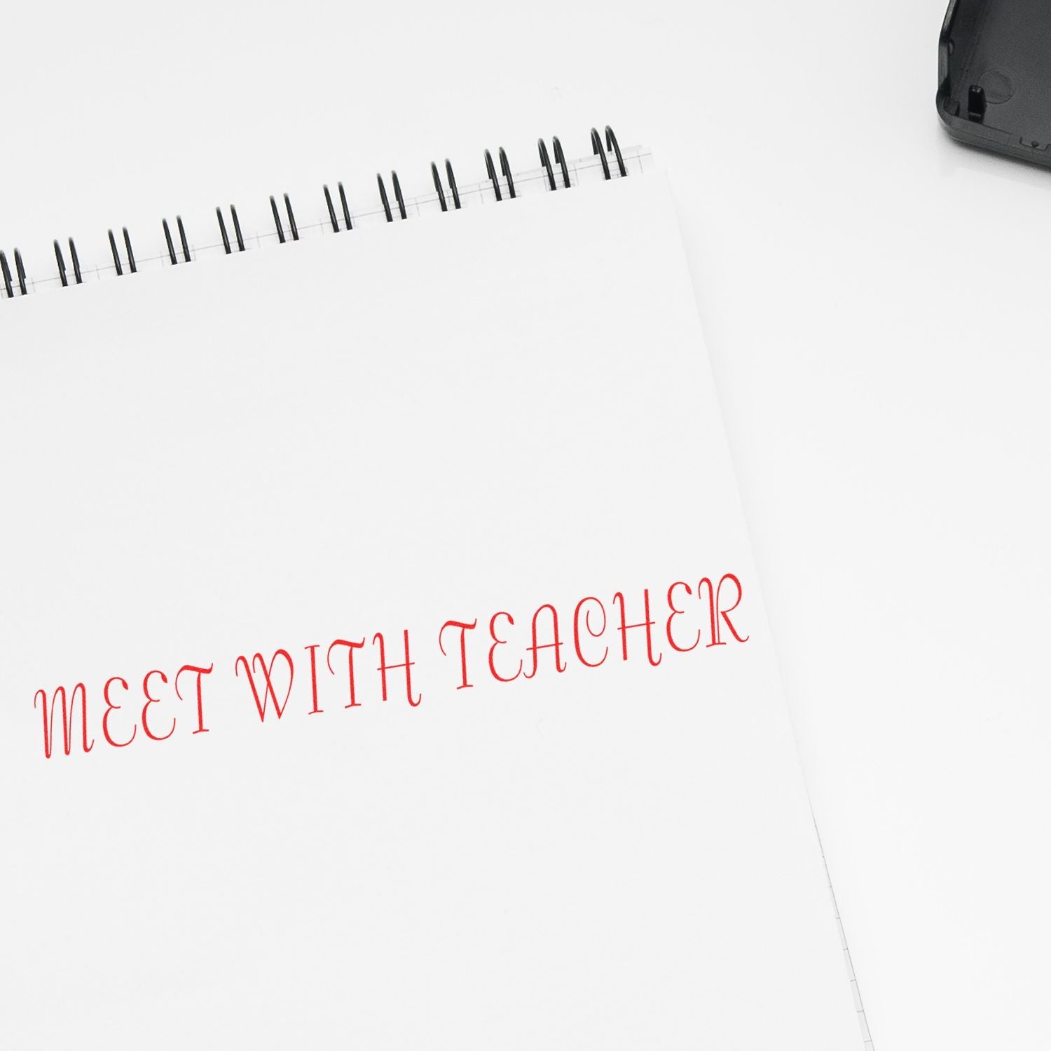 Self Inking Meet With Teacher Stamp in red ink on a white spiral notebook, with the stamp pad partially visible in the top right corner.