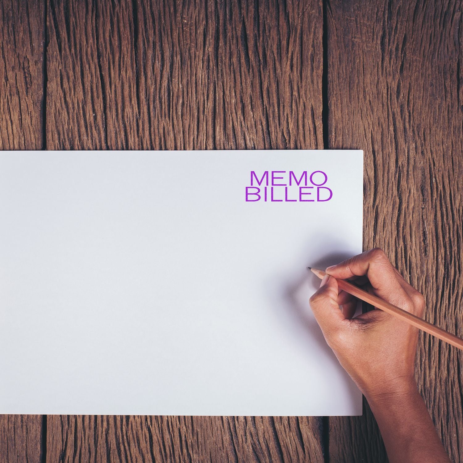 Hand holding pencil near white paper stamped with Memo Billed in purple ink on a wooden surface.