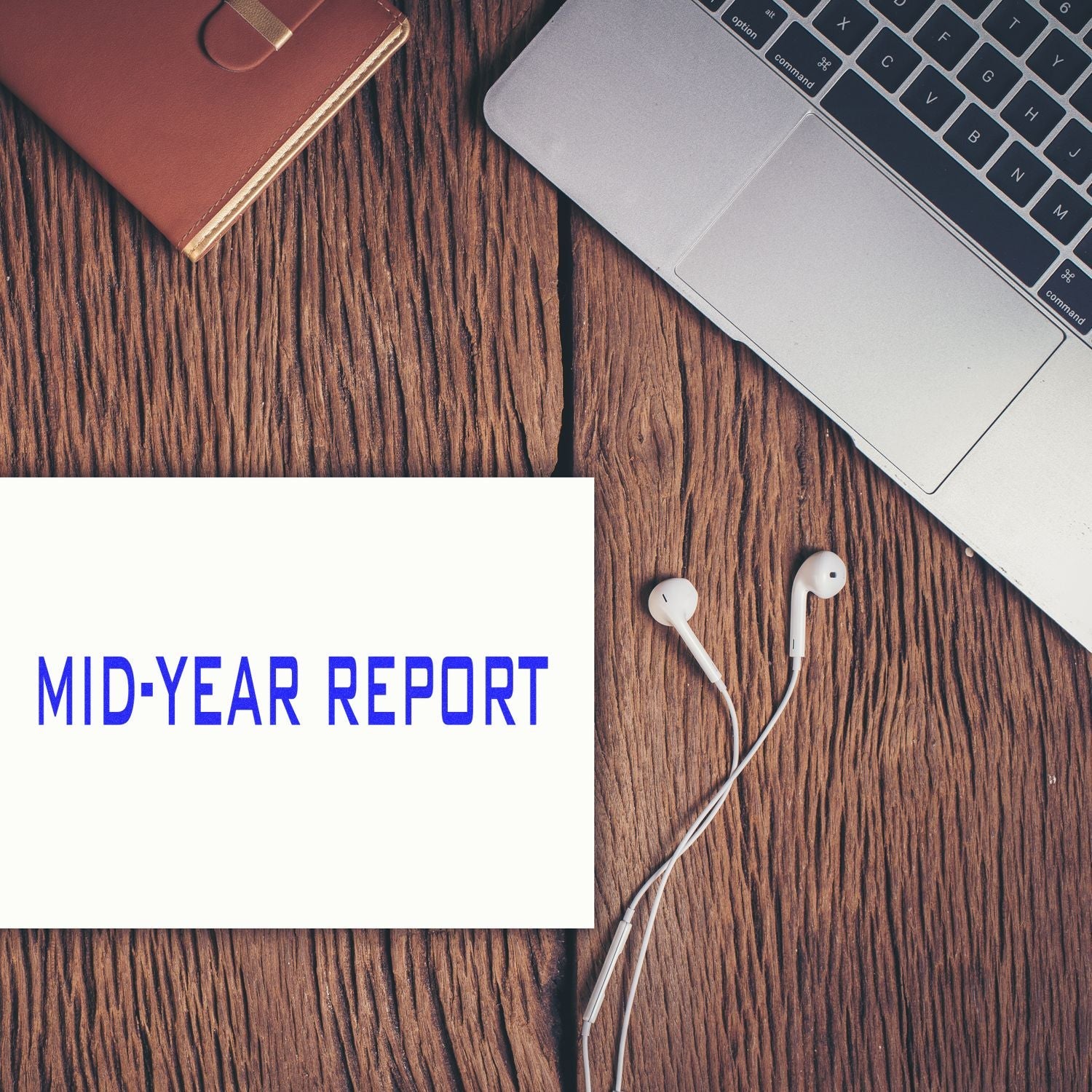 A Self Inking Mid Year Report Stamp on a wooden desk with a laptop, earphones, and a notebook.