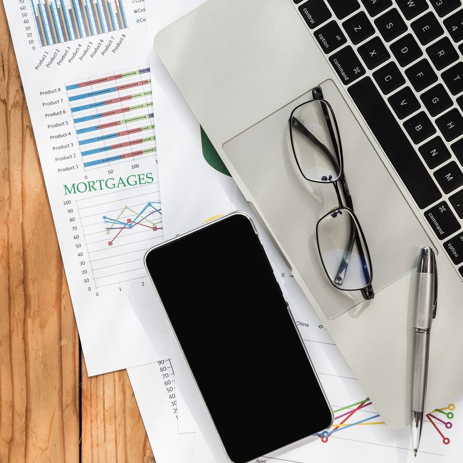 Mortgages rubber stamp on a document with charts, next to a laptop, glasses, smartphone, and pen on a wooden desk.