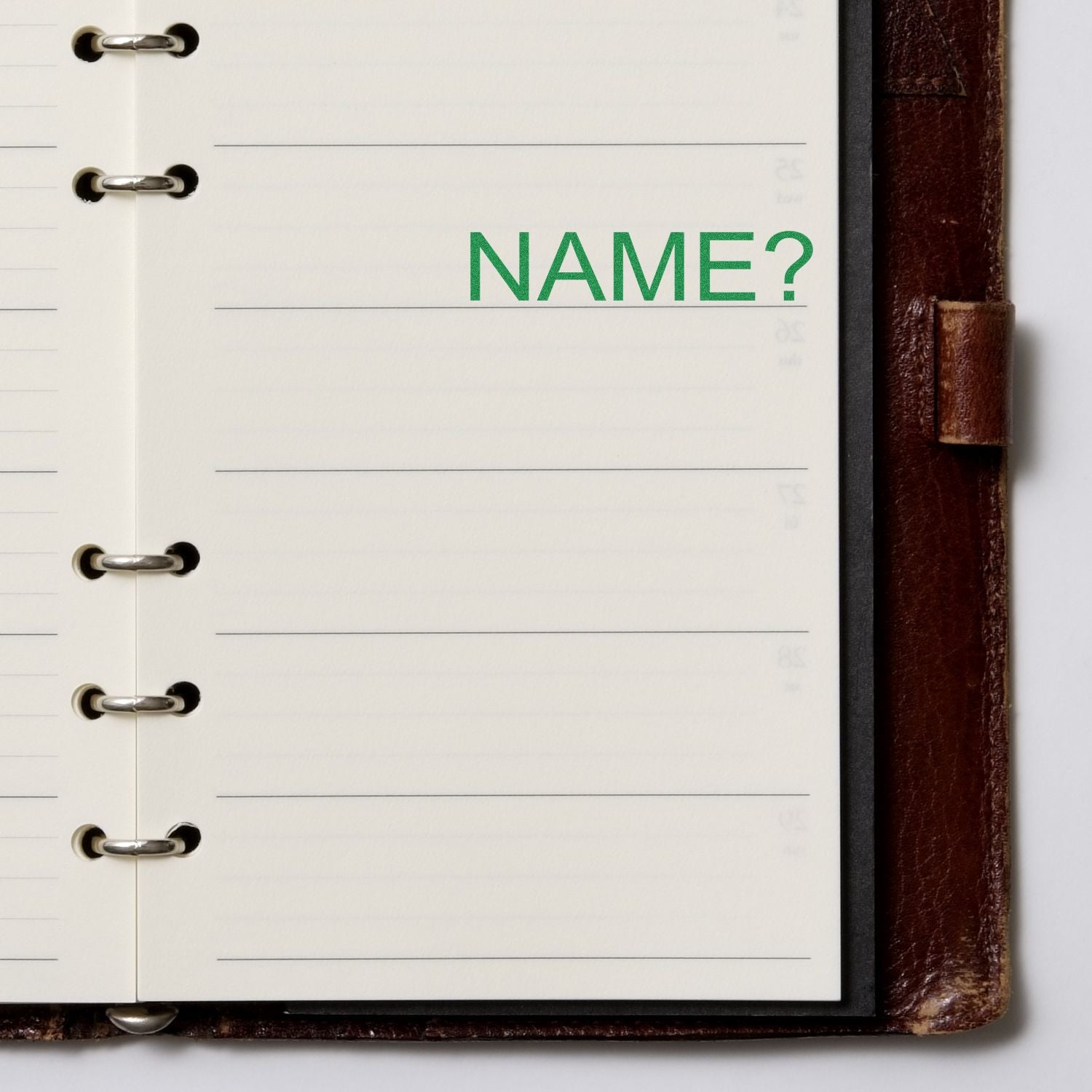 Self Inking Name Stamp used on a lined notebook page, leaving a green NAME? imprint. The notebook has a brown leather cover.