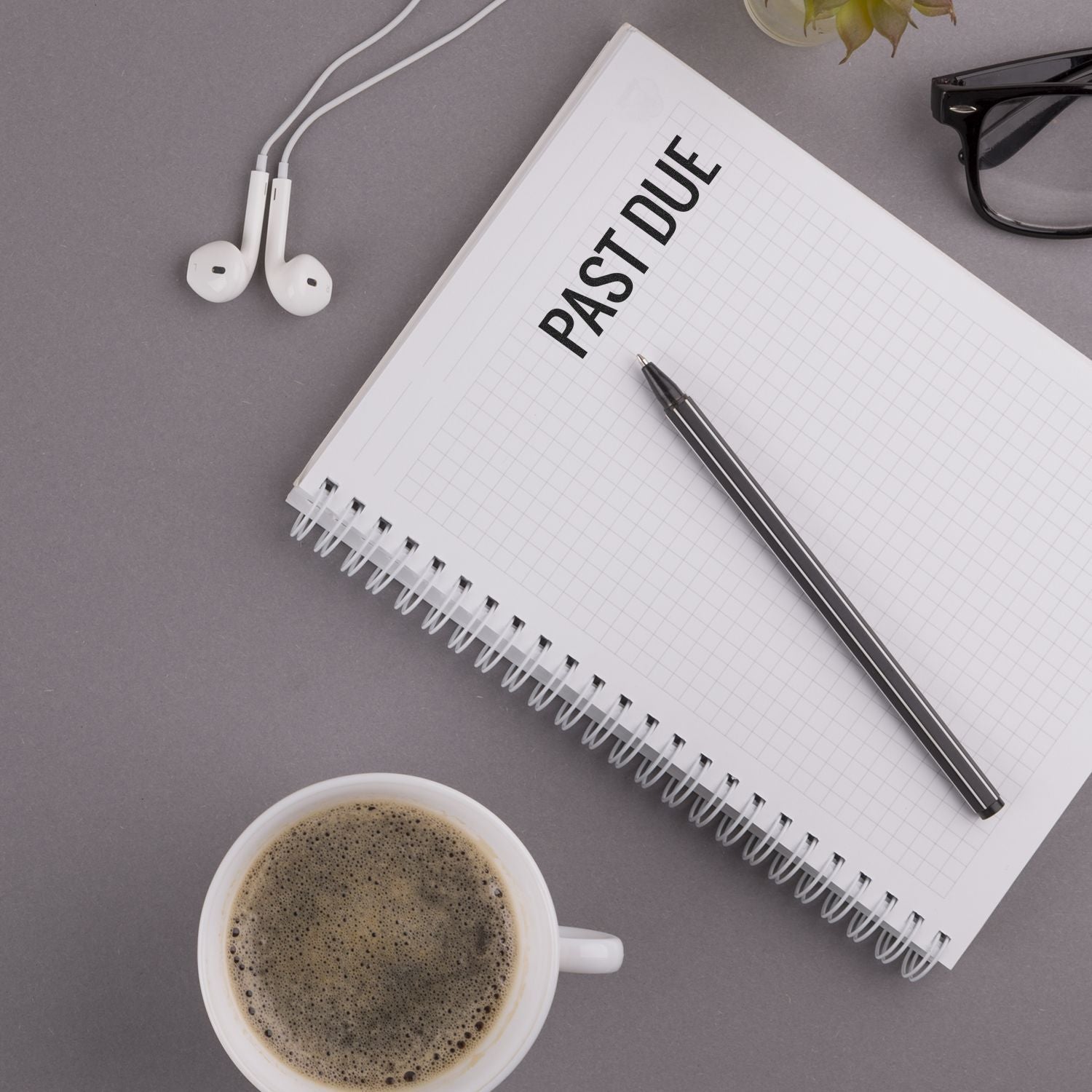 Notebook stamped with PAST DUE using a Narrow Bold Past Due Rubber Stamp, next to a pen, coffee cup, glasses, and earphones.