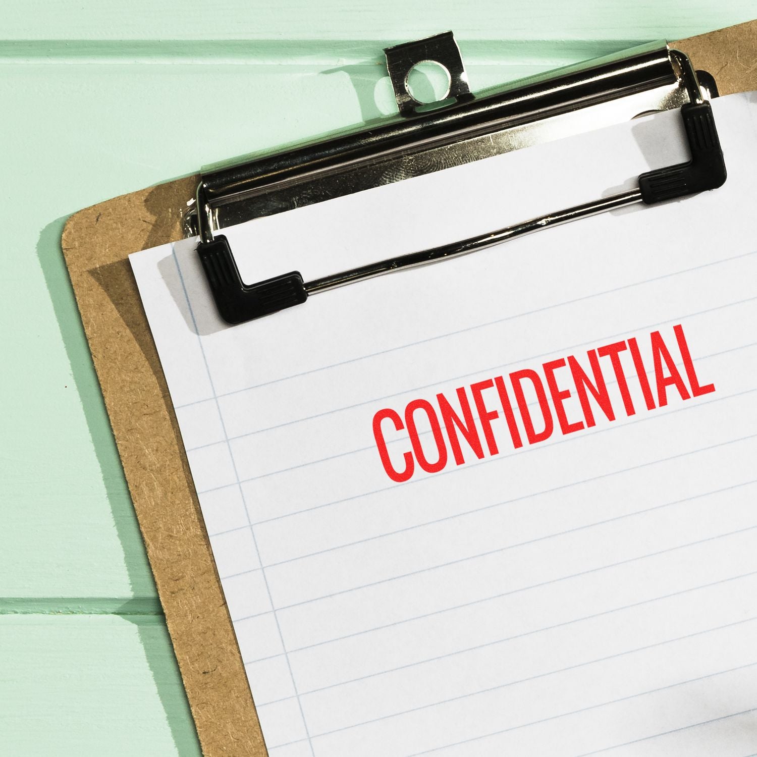 A clipboard with a lined paper stamped with a red CONFIDENTIAL using a narrow confidential rubber stamp.