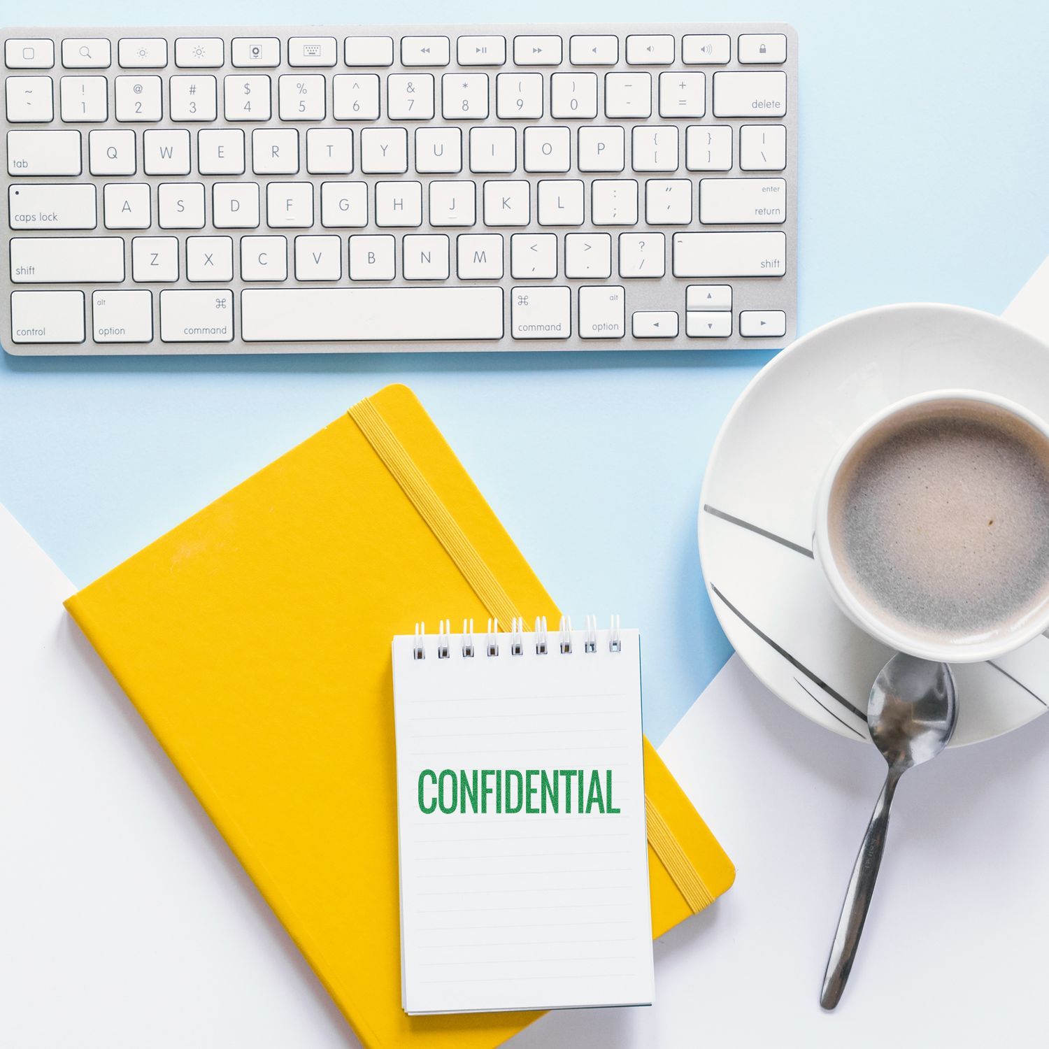 Narrow Confidential rubber stamp on a notepad beside a yellow notebook, keyboard, and coffee cup on a light blue and white background.