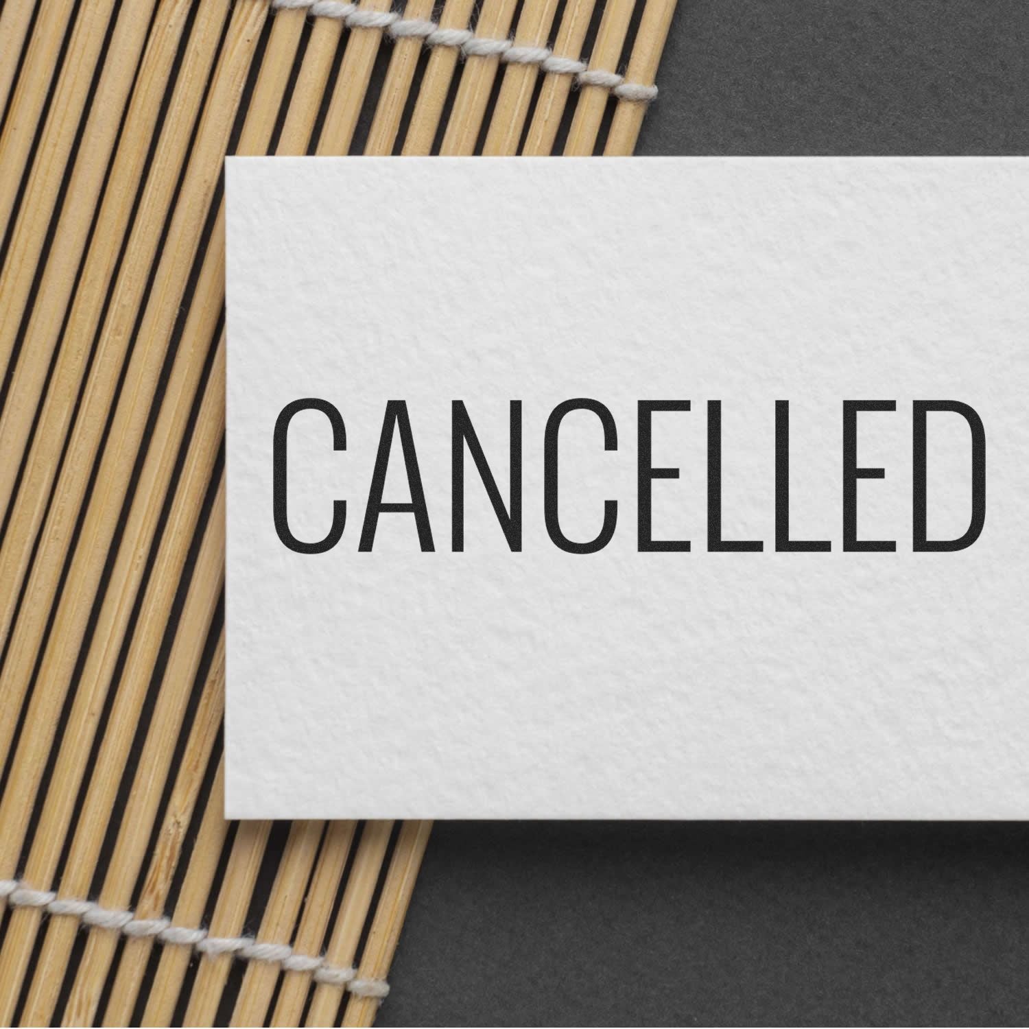 Narrow Font Cancelled Rubber Stamp on white card placed on a bamboo mat and dark background.