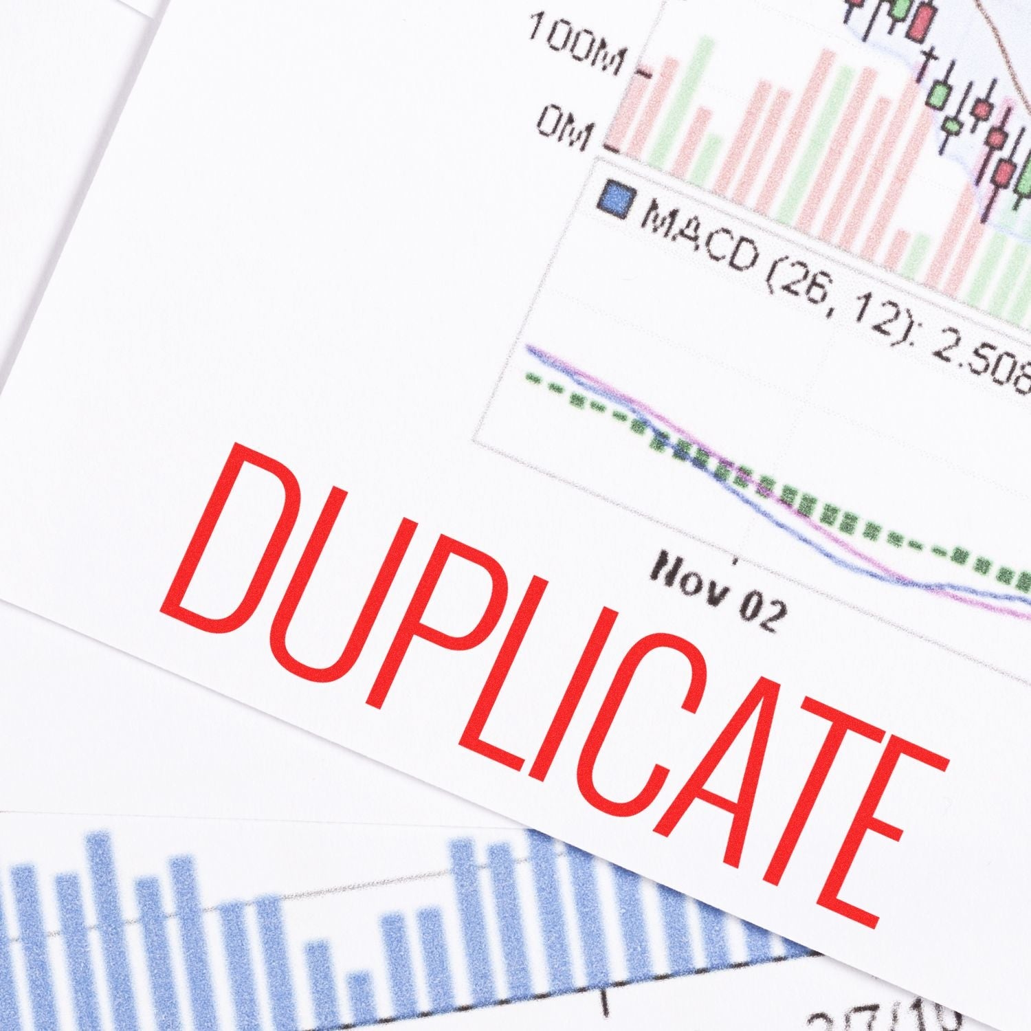 Self Inking Narrow Font Duplicate Stamp marking DUPLICATE in red ink on financial documents with graphs and charts in the background.