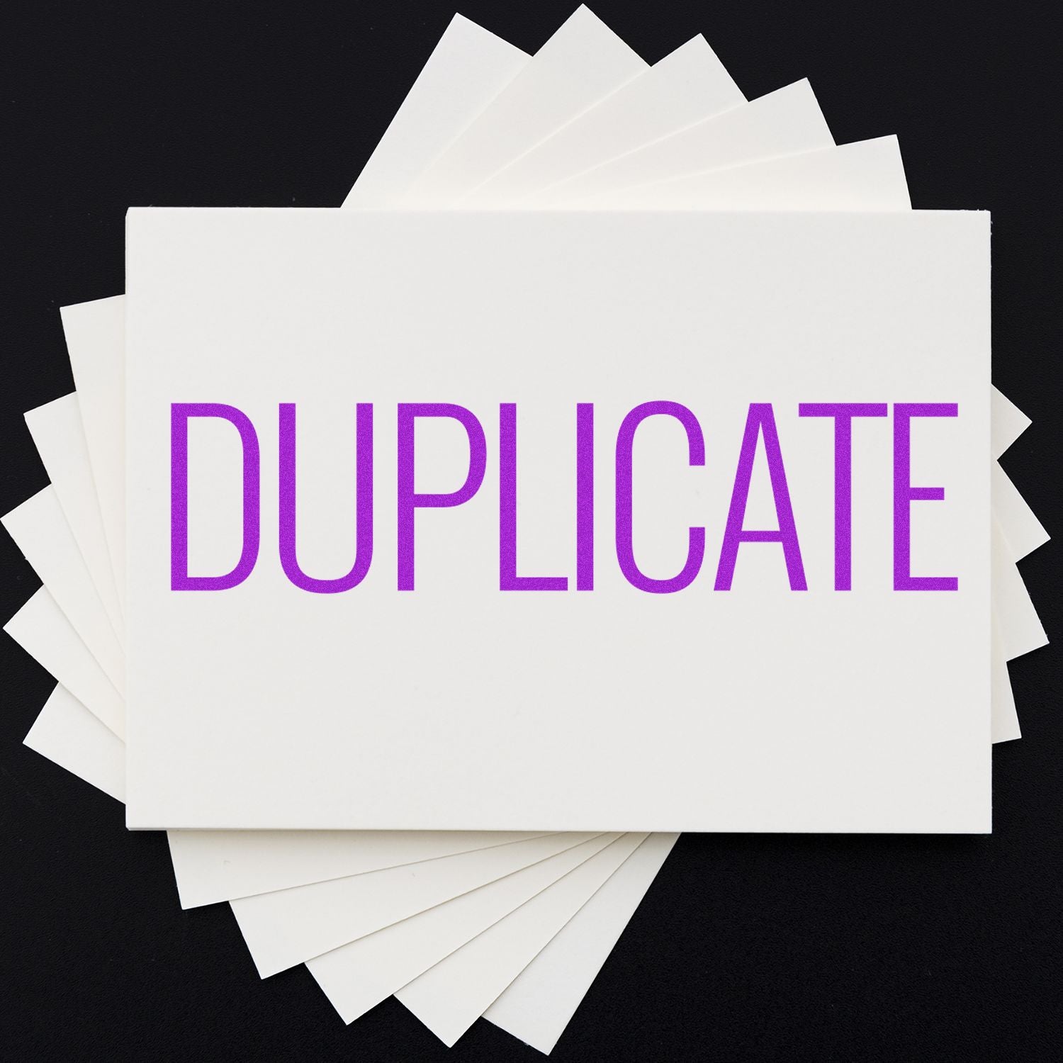 Self Inking Narrow Font Duplicate Stamp in use, stamping the word DUPLICATE in bold purple letters on white cards arranged in a fan shape.