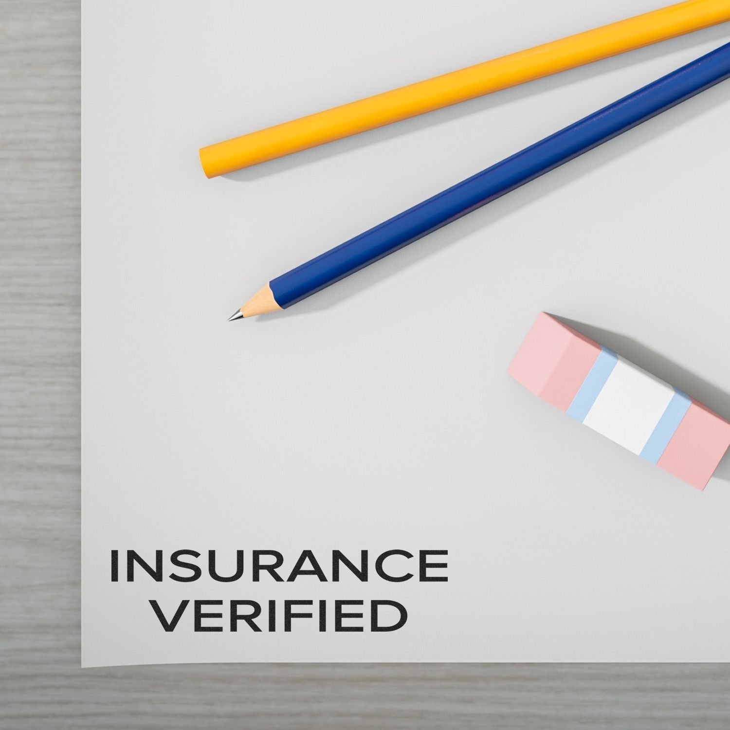 Slim Pre-Inked Narrow Font Insurance Verified Stamp on paper with yellow and blue pencils and a pink eraser on a desk.