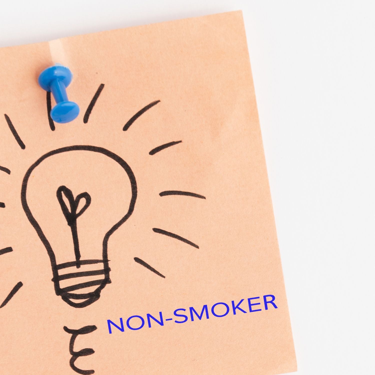 A brown paper with a lightbulb drawing pinned by a blue pushpin, stamped with NON-SMOKER in a narrow font.