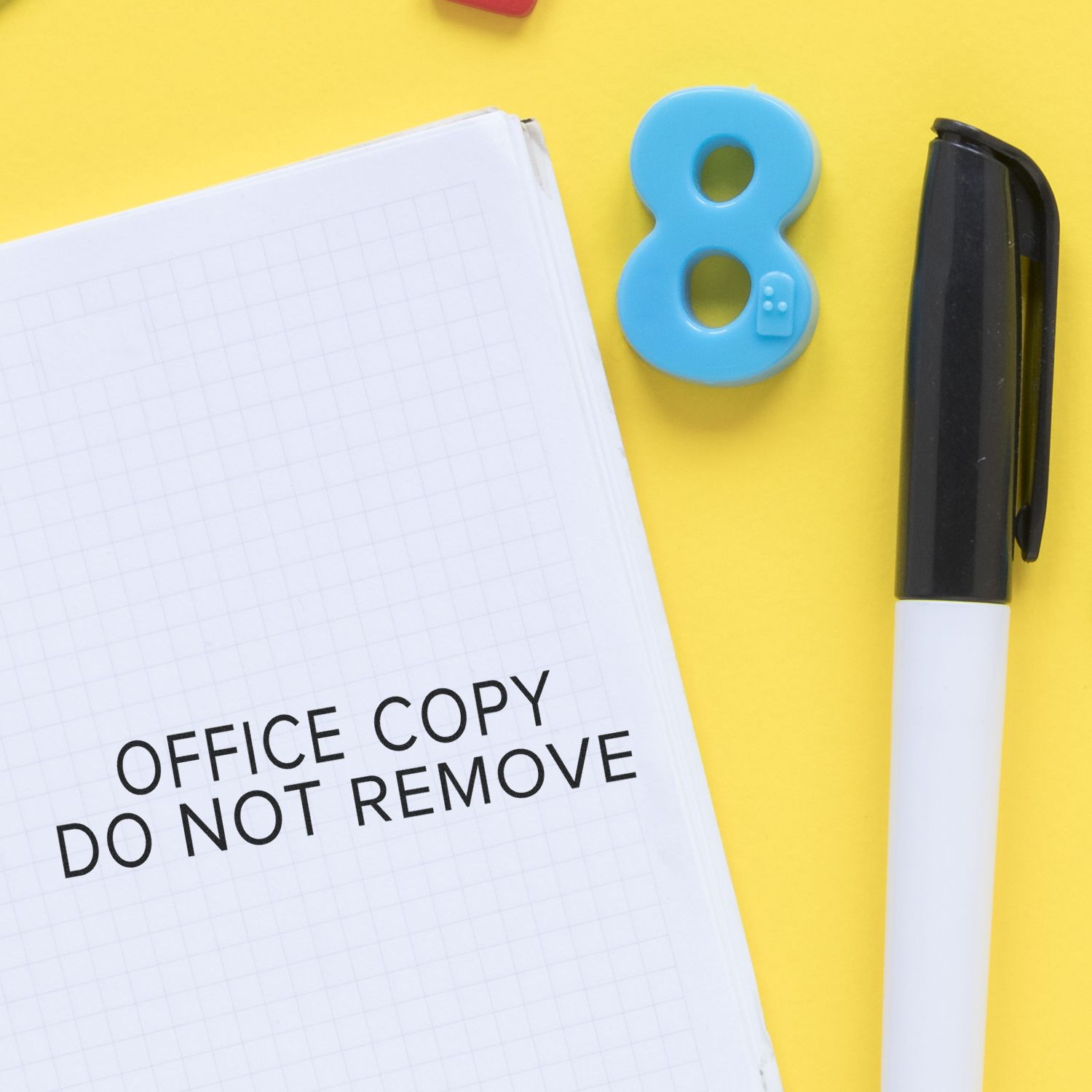 Narrow Font Office Copy Do Not Remove Rubber Stamp on a notebook next to a pen and a blue number 8 on a yellow background.