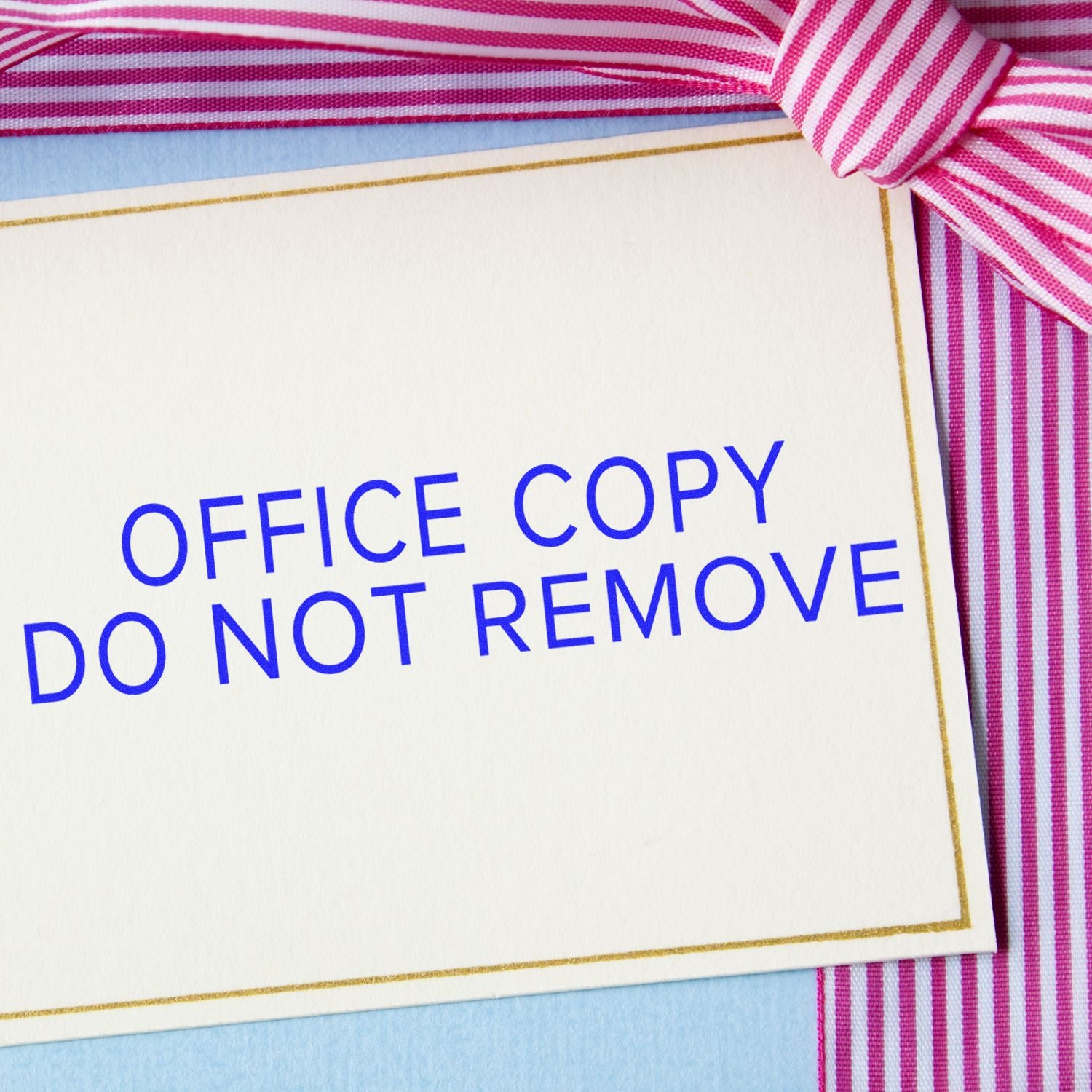 Narrow Font Office Copy Do Not Remove Rubber Stamp on a white card with a pink and white striped ribbon in the background.