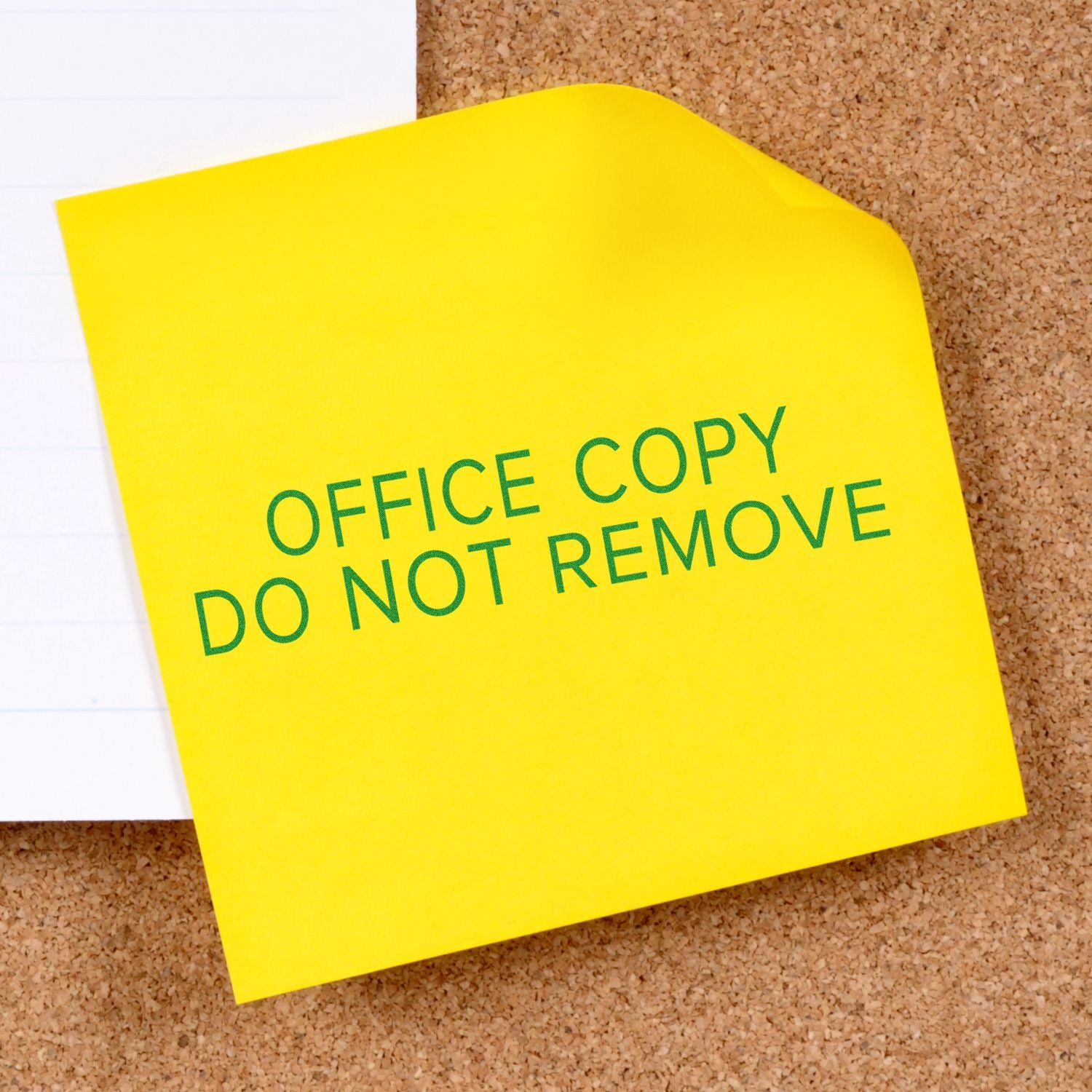 Yellow sticky note with OFFICE COPY DO NOT REMOVE stamped in green narrow font, pinned on a corkboard.