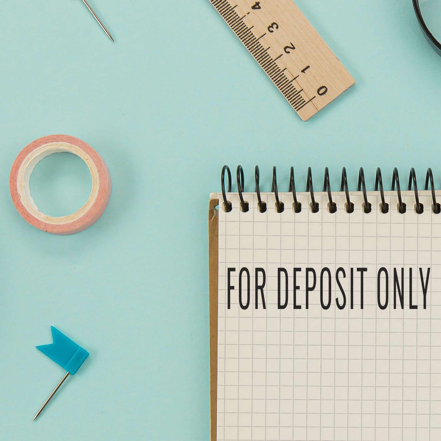 Large Narrow For Deposit Only Self-Inking Stamp in use on a notebook, surrounded by office supplies on a light blue background.