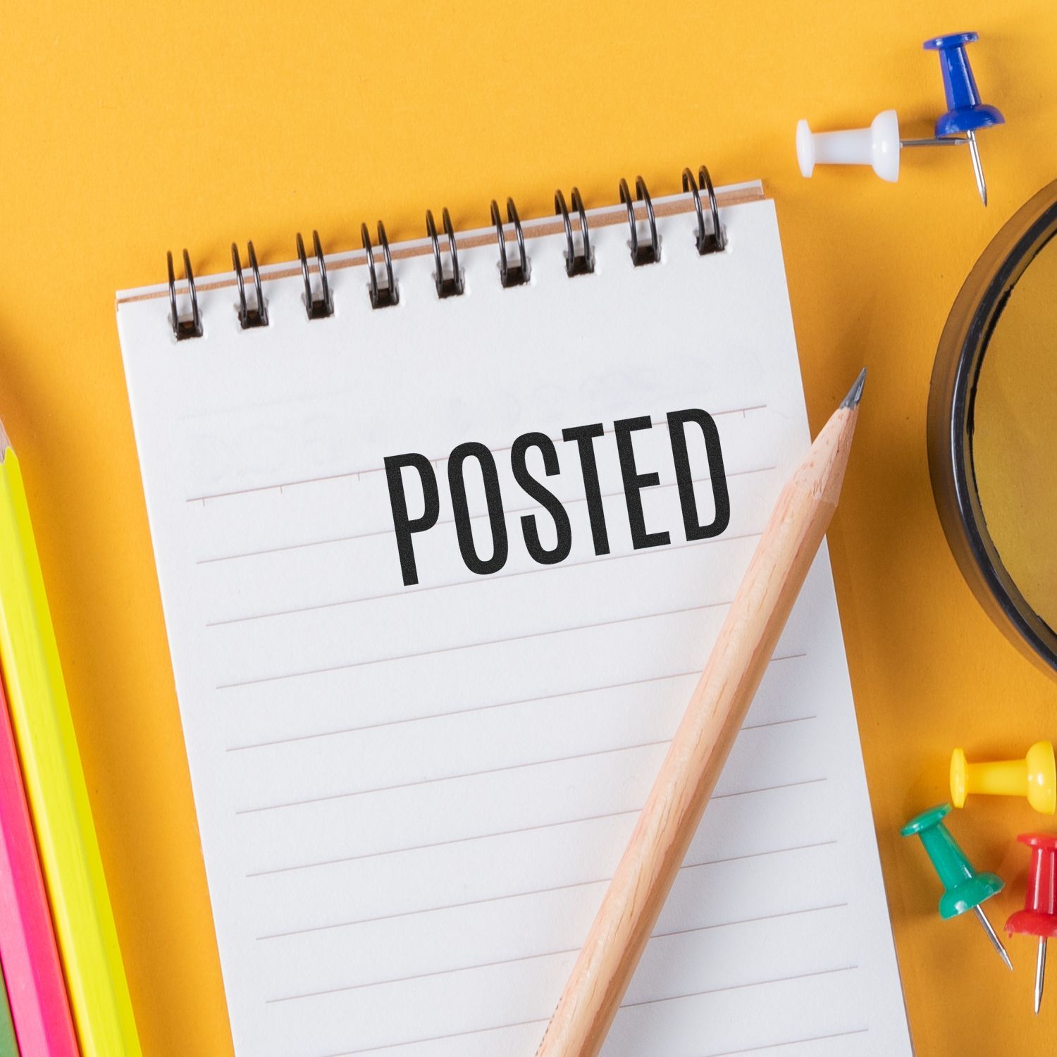 Narrow Posted Rubber Stamp on a spiral notebook with a pencil, colorful push pins, and a magnifying glass on a yellow background.