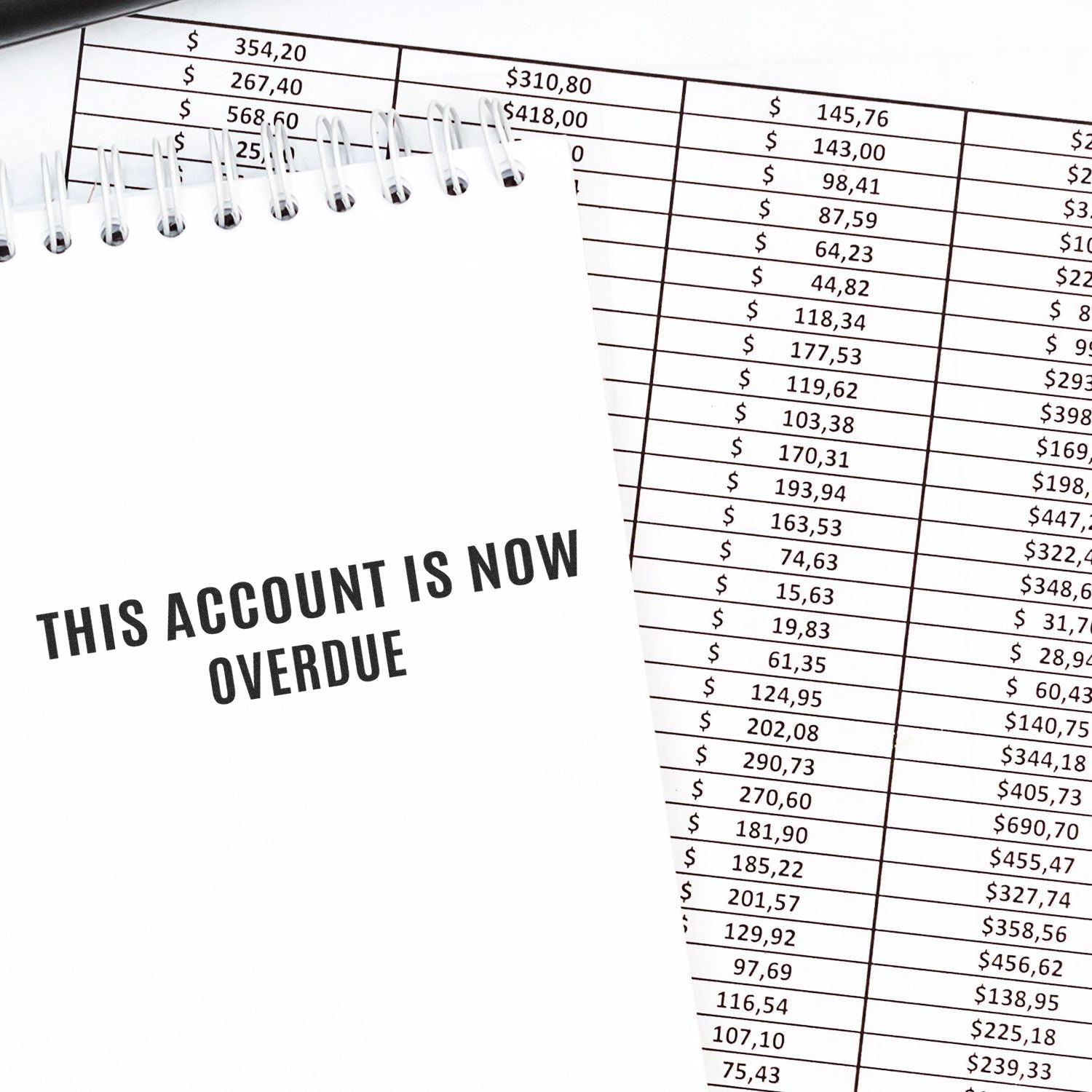 Self Inking Narrow This account is now overdue Stamp used on a white notepad, placed over a financial document with numbers.