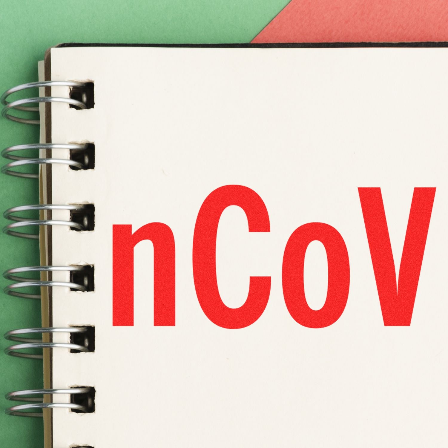 Spiral notebook with 'nCoV' stamped in bold red letters, using an nCov Rubber Stamp, on a green and red background.