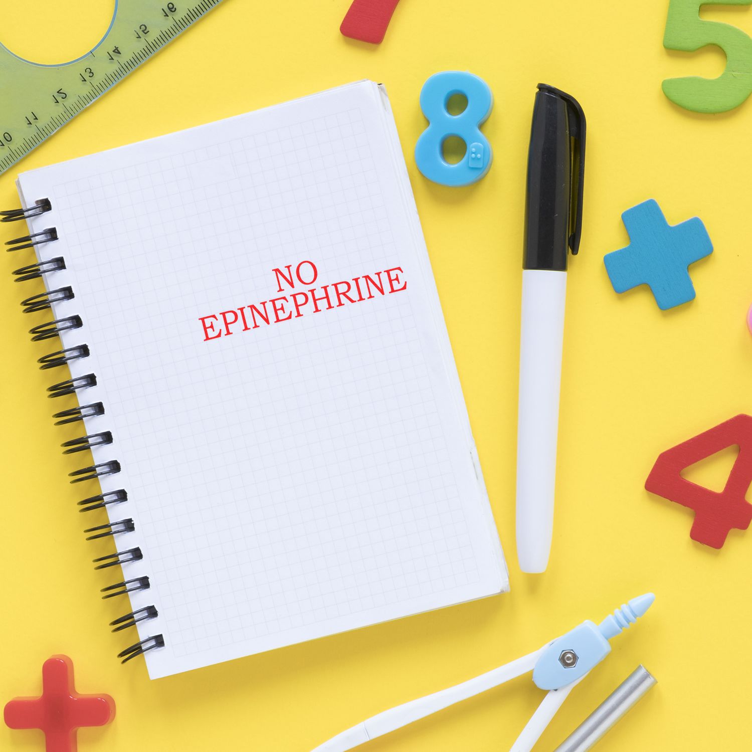 No Epinephrine Medical Rubber Stamp on a notebook surrounded by colorful numbers, a pen, ruler, and other stationery on a yellow background.