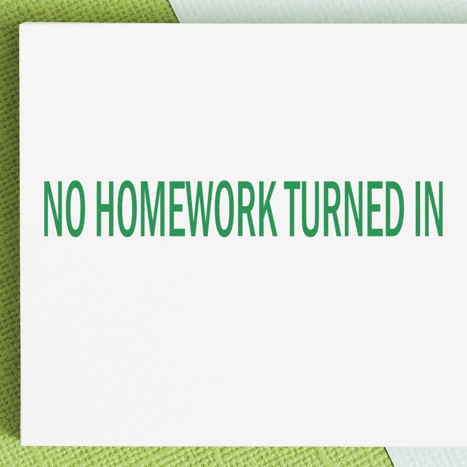 No Homework Turned In rubber stamp in green ink on white paper, placed on a green textured surface.