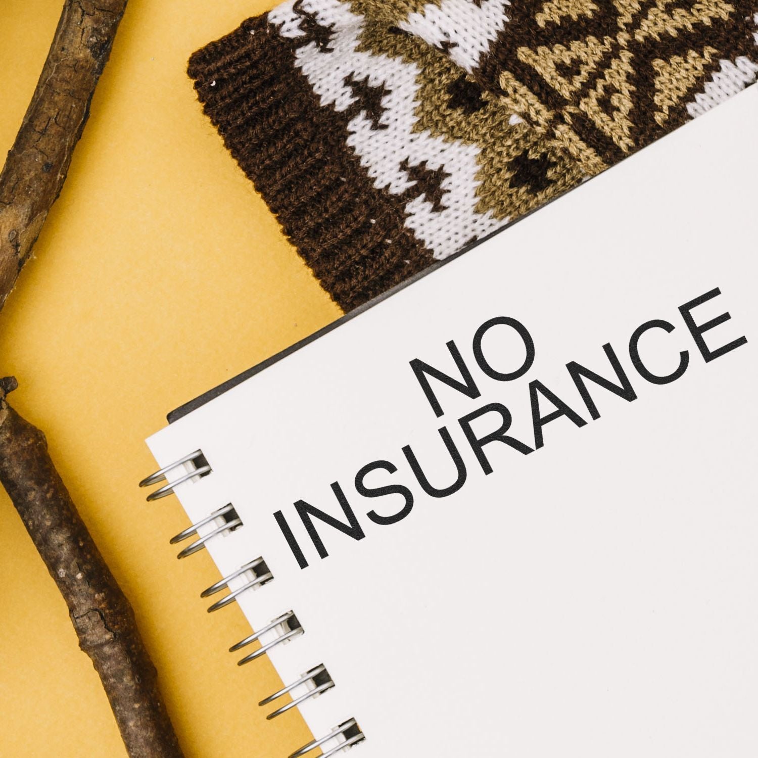 No Insurance rubber stamp on a white notebook page with a knitted item and wooden sticks in the background.