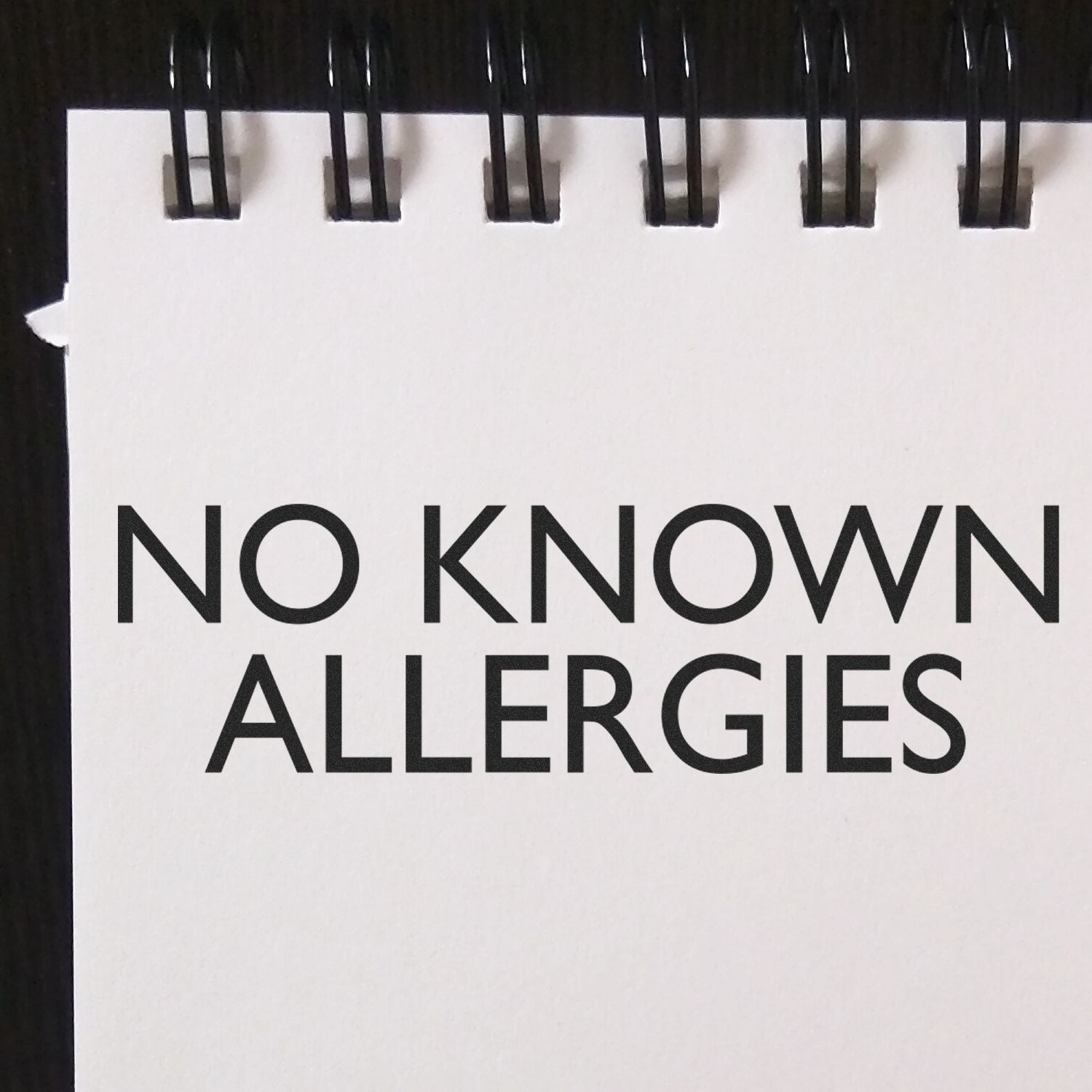 No Known Allergies Rubber Stamp impression on a white notepad with black spiral binding.