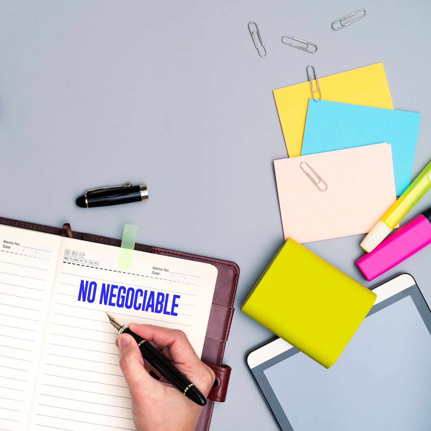 Hand stamping No Negociable in blue ink on a notebook, surrounded by colorful sticky notes, paper clips, and stationery.