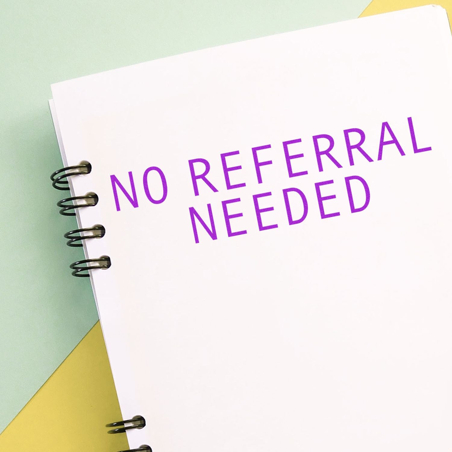 Large Self Inking No Referral Needed Stamp used on a white spiral notebook with purple text NO REFERRAL NEEDED on a pastel background.