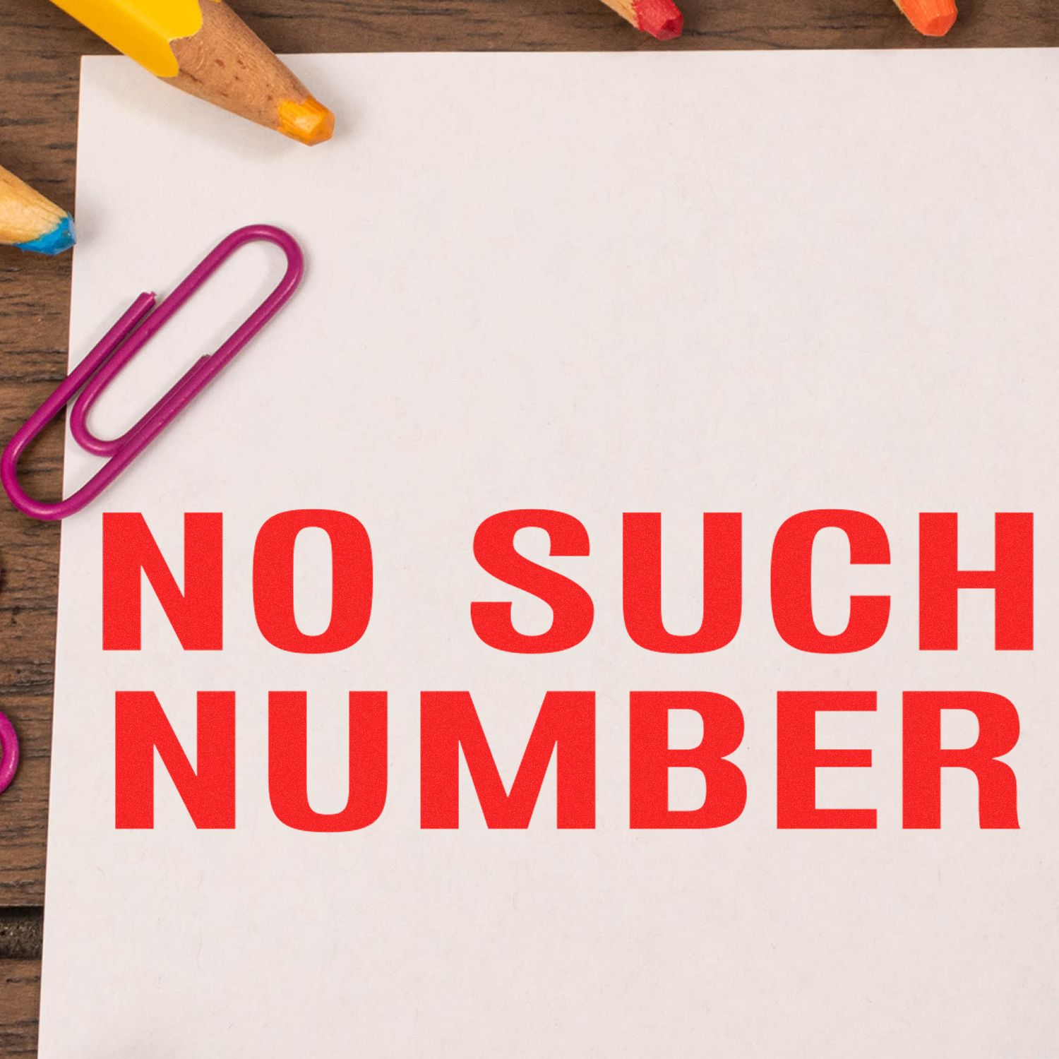 No Such Number Rubber Stamp in red ink on white paper, surrounded by colorful paperclips and pencils on a wooden surface.