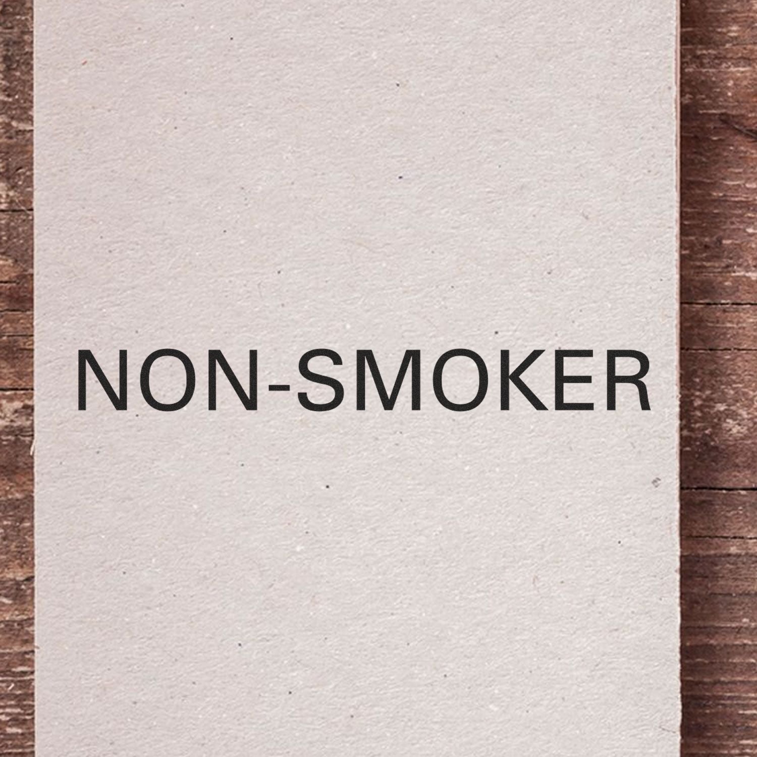 Non-Smoker Rubber Stamp impression on a piece of paper, displaying the text 'NON-SMOKER' in bold black letters on a wooden surface."