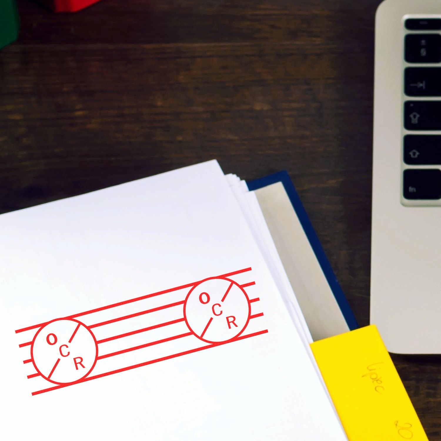 Self Inking OCR Stamp imprint in red on a white paper beside a laptop and yellow sticky notes on a wooden desk.