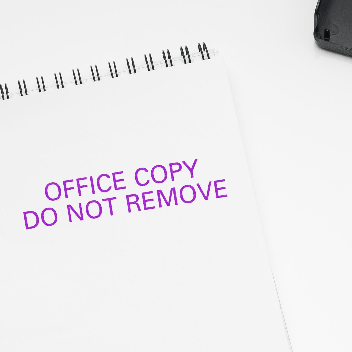 Self Inking Office Copy Do Not Remove Stamp in purple ink on a white spiral notebook, with part of the stamp visible in the top right corner.