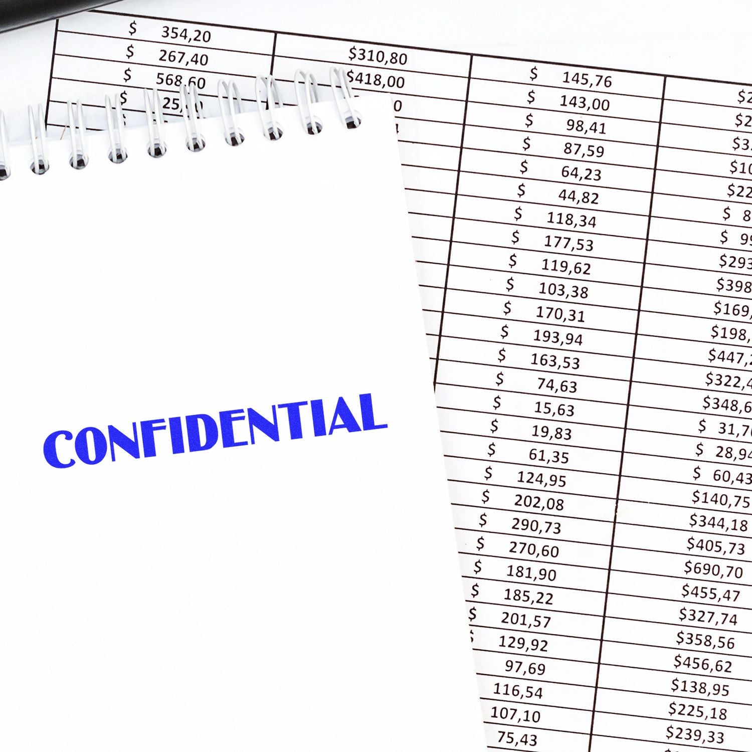 Slim Pre-Inked Optima Confidential Stamp in blue ink on a white notepad, placed over a financial spreadsheet.