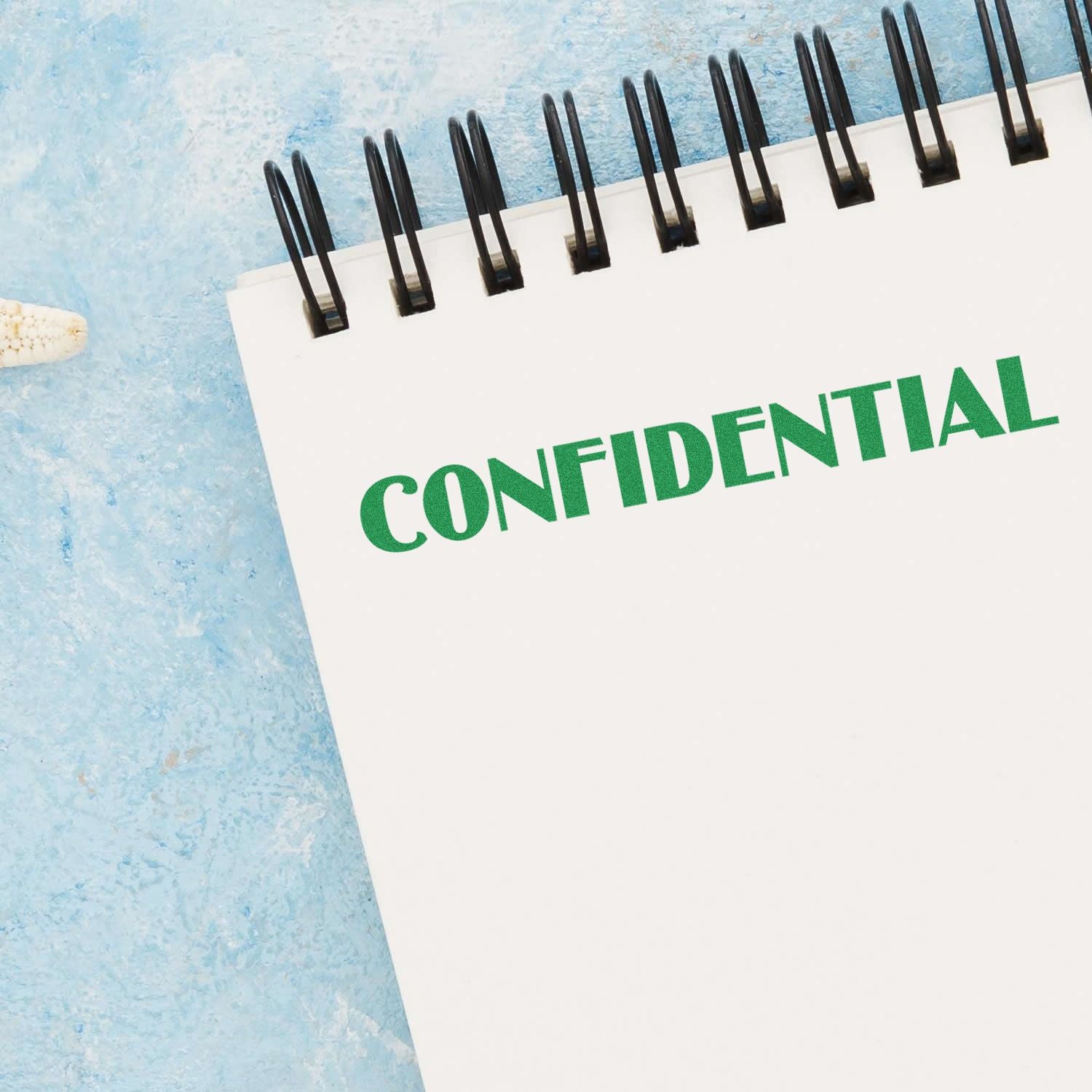 Notebook with 'CONFIDENTIAL' stamped in green using an Optima Confidential Rubber Stamp on a blue textured background.