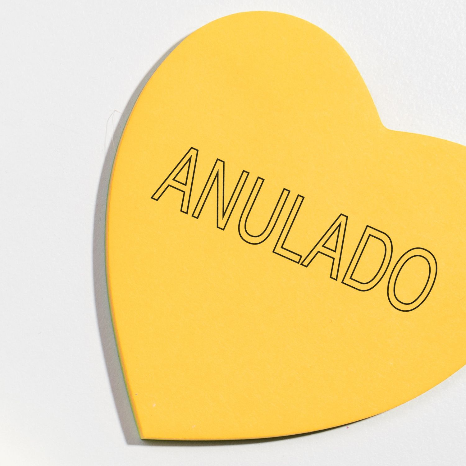 Yellow heart-shaped paper with ANULADO stamped in black outline letters using an Outline Anulado Rubber Stamp.