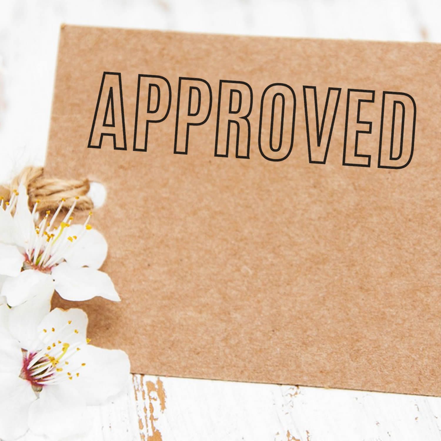 Outline Approved Rubber Stamp on a brown card with white flowers on a rustic white wooden surface.