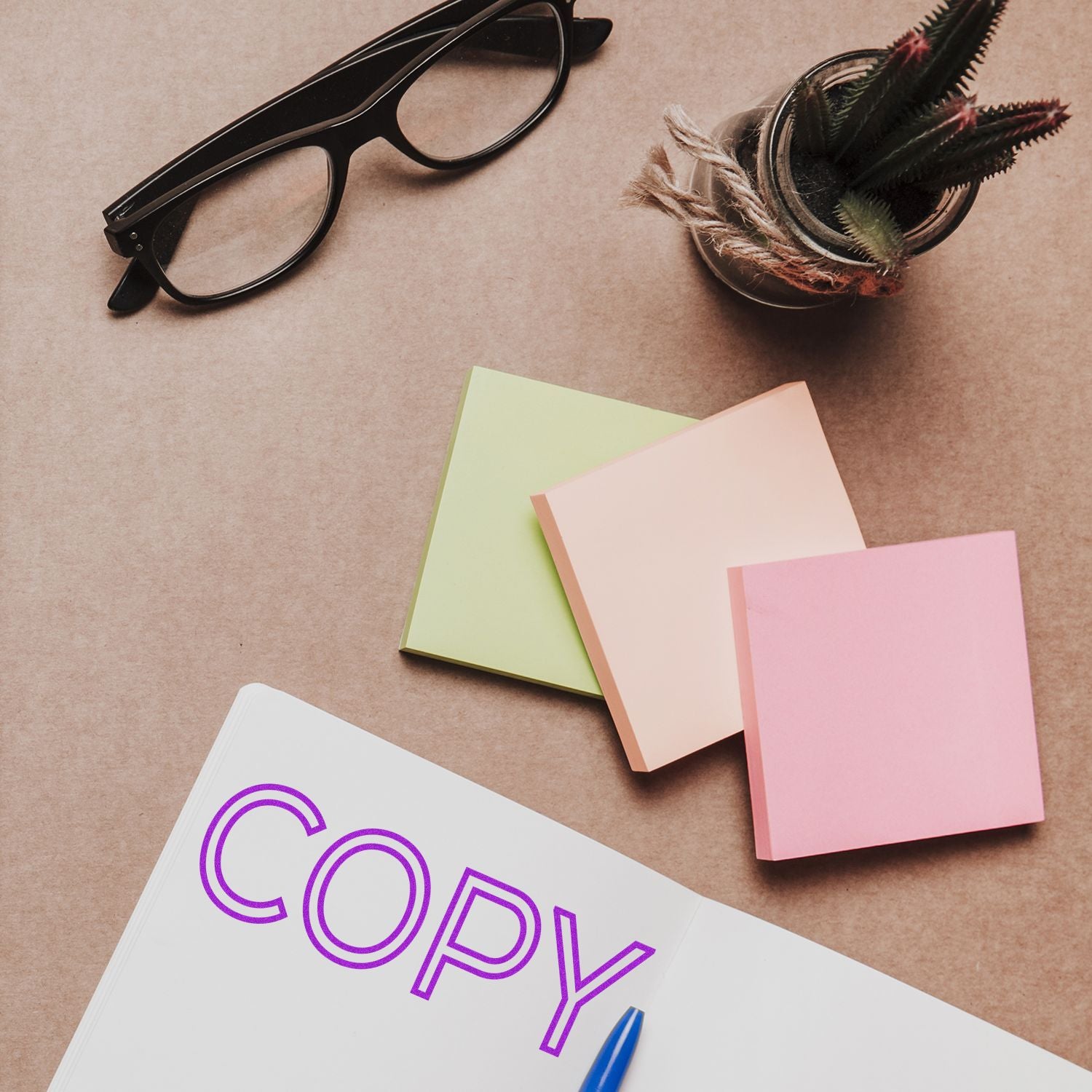 Large Outline Copy Rubber Stamp used on a notebook, with glasses, sticky notes, and a plant on a brown desk.