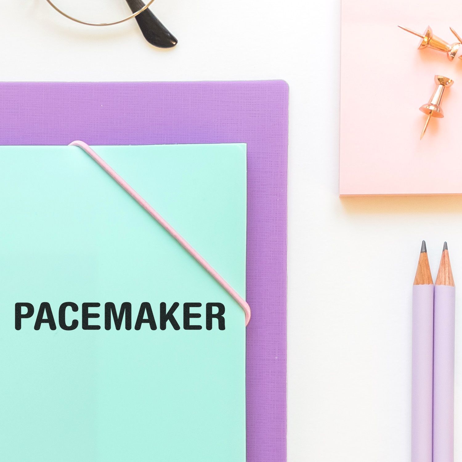 Large Self Inking Pacemaker Stamp in use on a mint green folder, surrounded by office supplies including pencils, push pins, and glasses.