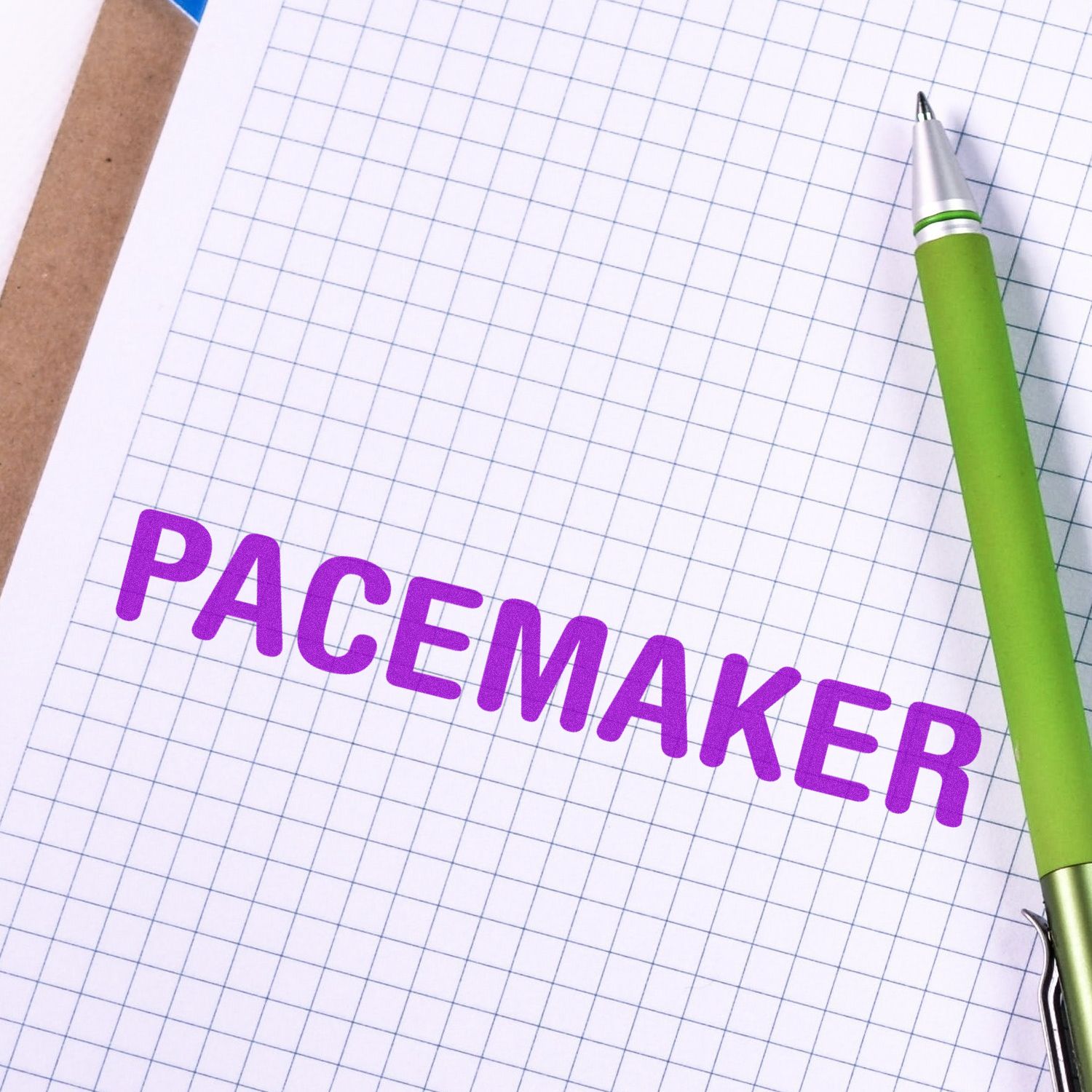 Self Inking Pacemaker Stamp imprinting PACEMAKER in purple ink on a grid paper, with a green pen placed beside the stamped text.