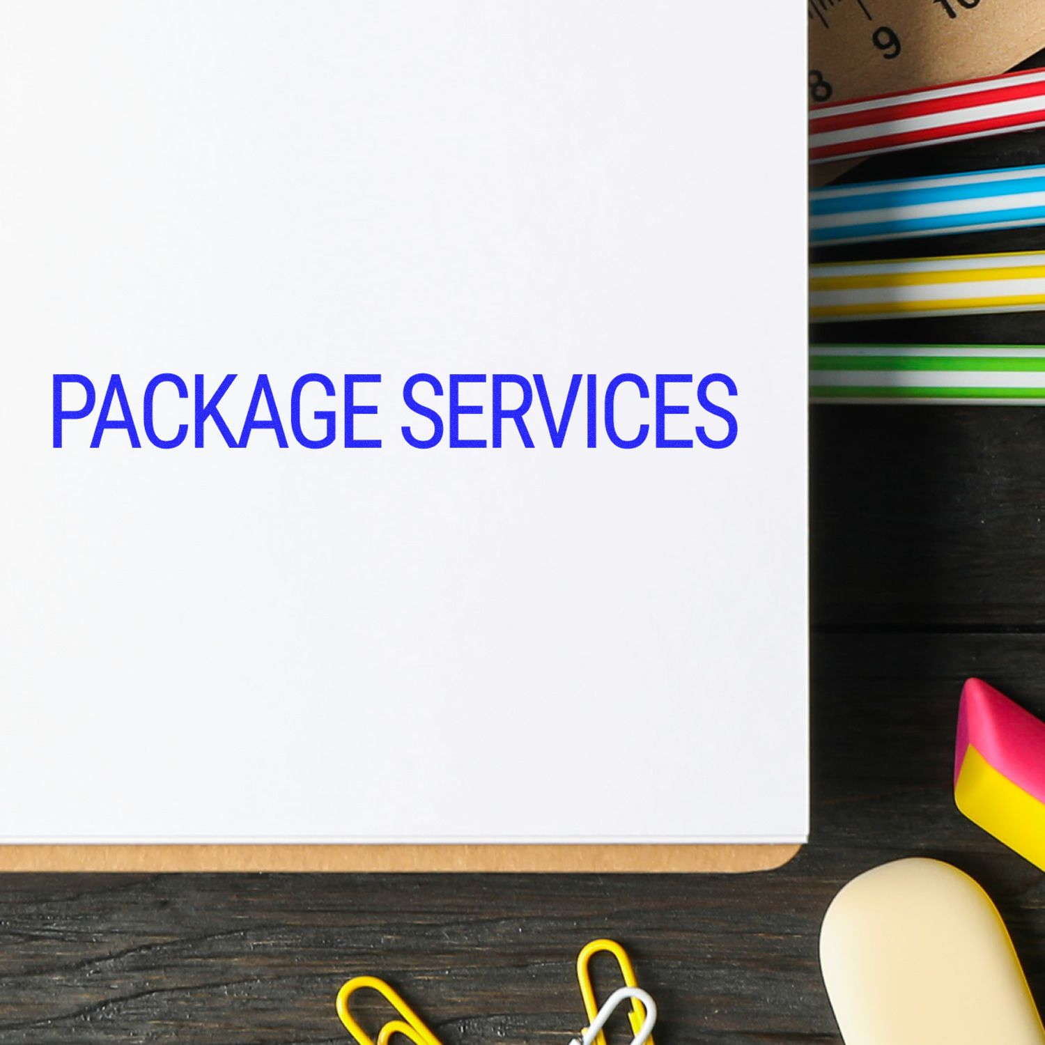 Self Inking Package Services Stamp marking PACKAGE SERVICES on a white paper, surrounded by colorful office supplies.