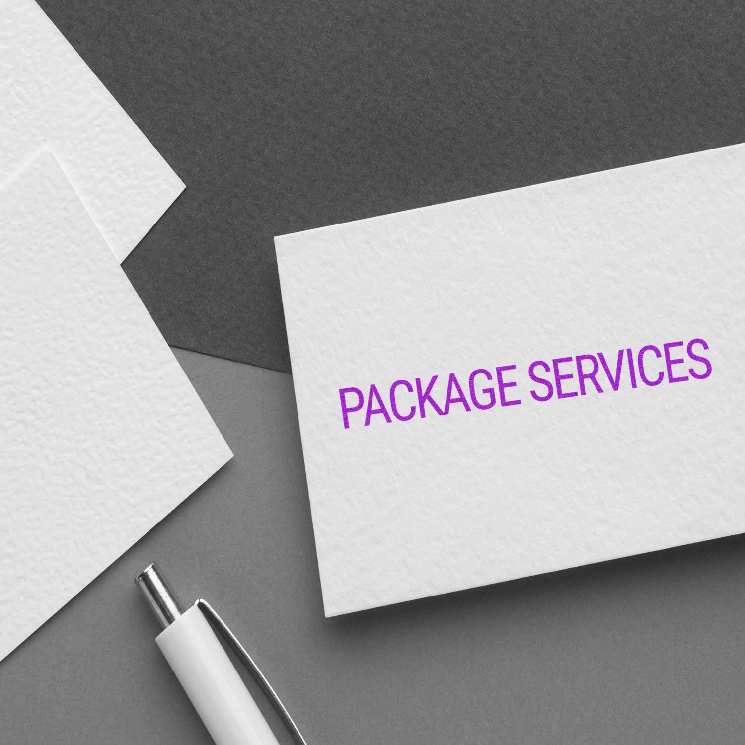 Self Inking Package Services Stamp used on a white card with PACKAGE SERVICES in purple text, placed on a gray surface with a pen nearby.