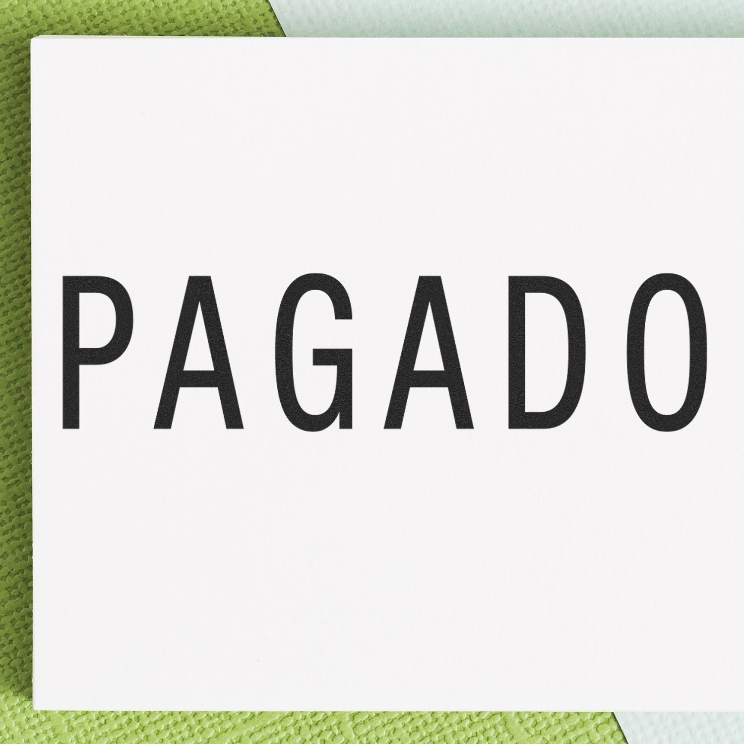 Large Pagado Rubber Stamp imprint on white paper, placed on a green textured surface.